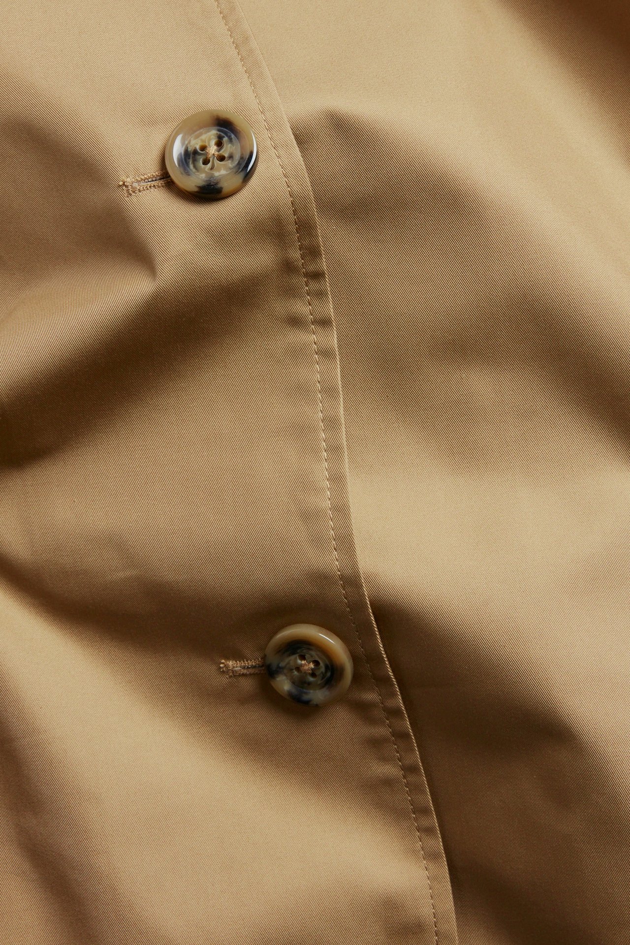 Zbliżenie beżowego płaszcza carcoat z listwą guzikową i dwoma guzikami we wzór szylkretu.