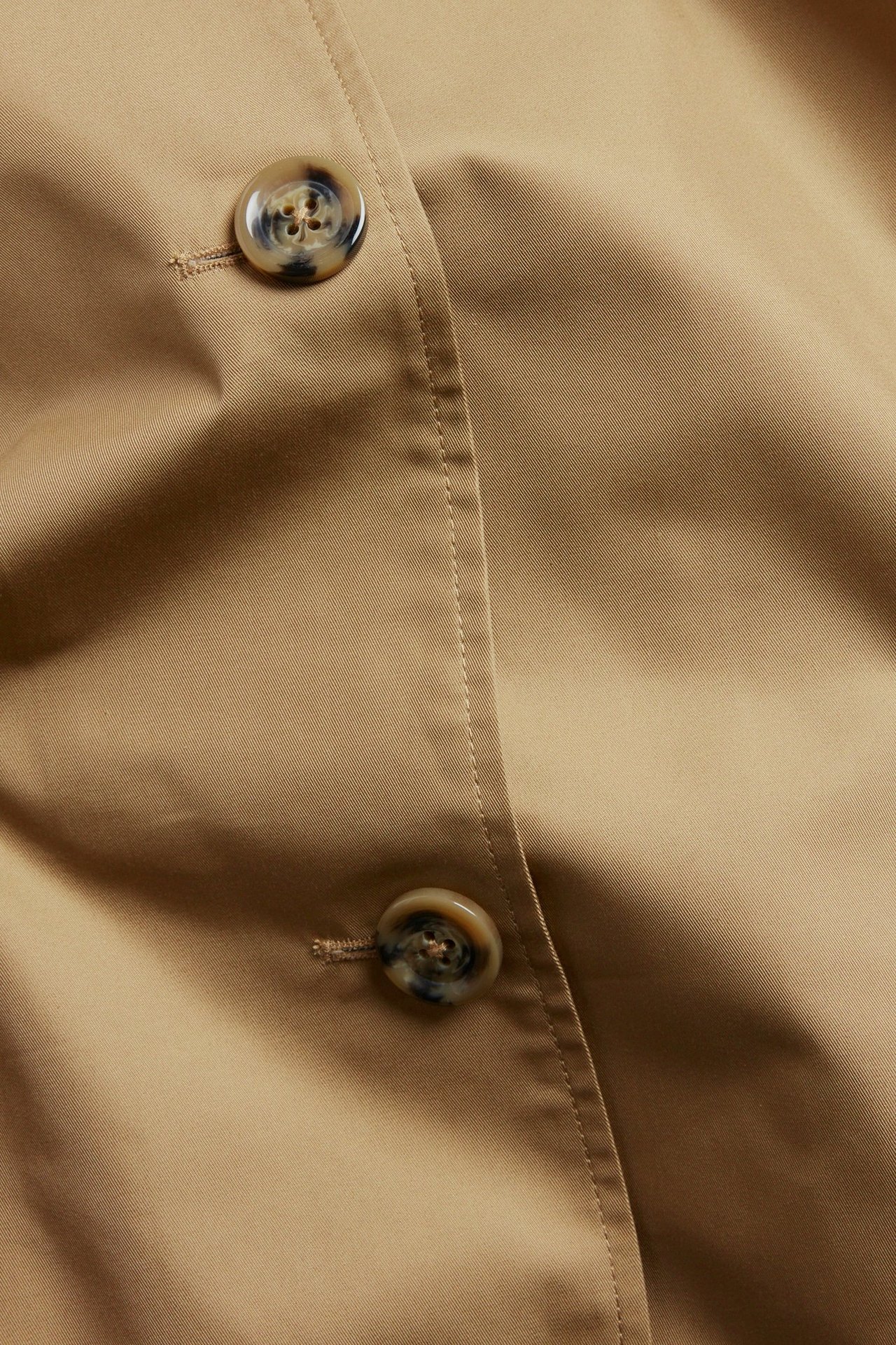 Zbliżenie beżowego płaszcza carcoat z listwą guzikową i dwoma guzikami we wzór szylkretu.
