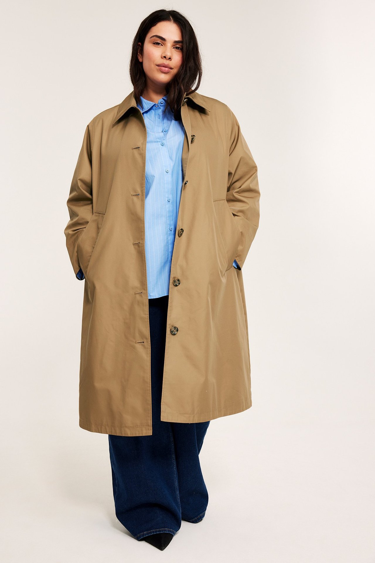 Kobieta z przodu: beżowy carcoat, jasnoniebieska koszula w paski, ciemnoniebieskie szerokie dżinsy.