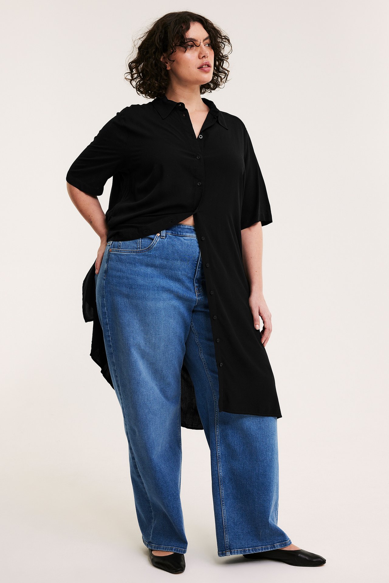 Nainen edestä: musta lyhythihainen viskoosipaitamekko, siniset leveälahkeiset farkut ja mustat ballerinat.