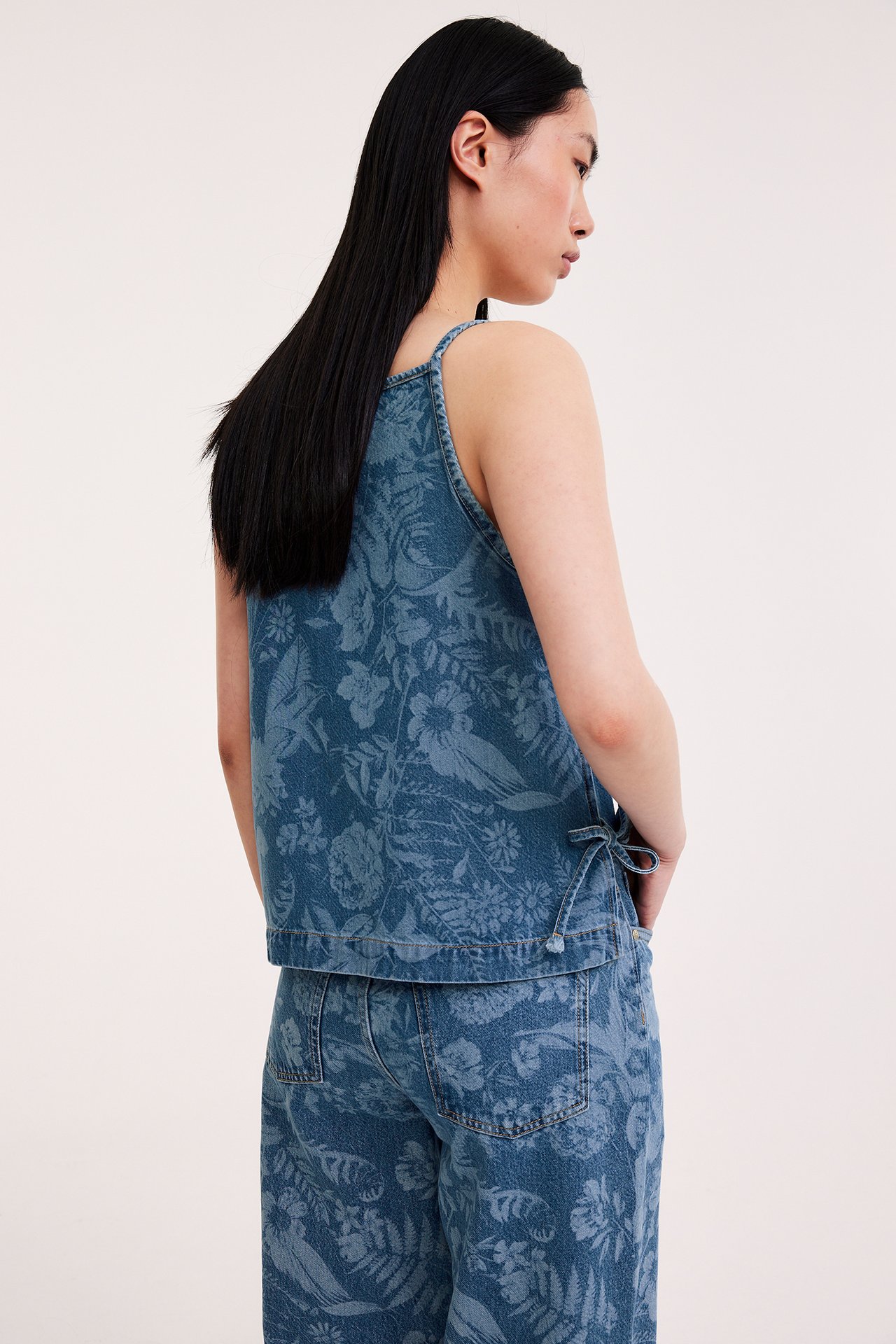 Sidan av en kvinna i ett ljusblått blommigt denimlinne med sidosnören och matchande blommiga jeans.