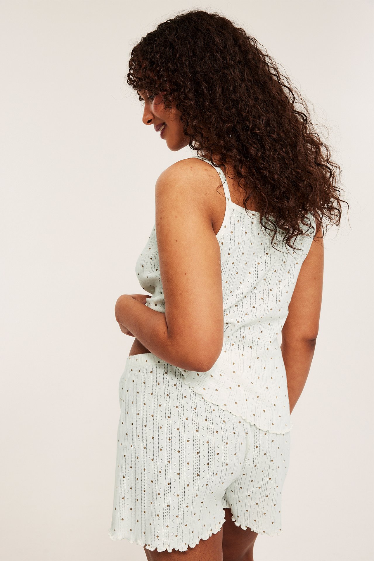 Side-bakfra av kvinne i beige pyjamassett i bomull pointelle med topp og shorts, prikket.