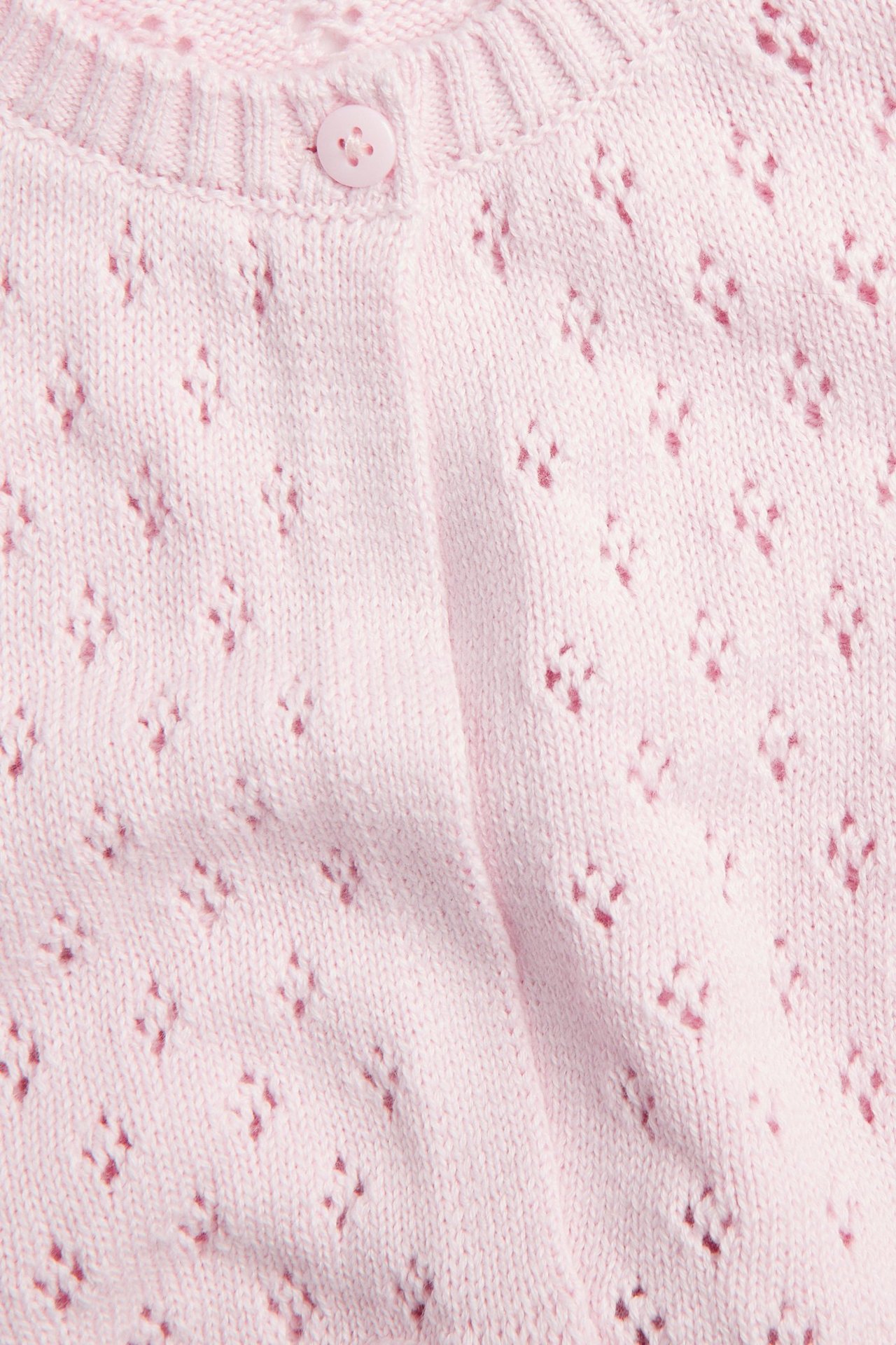 Zbliżenie na przód jasnoróżowego dzianinowego bawełnianego kardiganu z ażurowym wzorem i guzikiem przy prążkowanym dekolcie.
