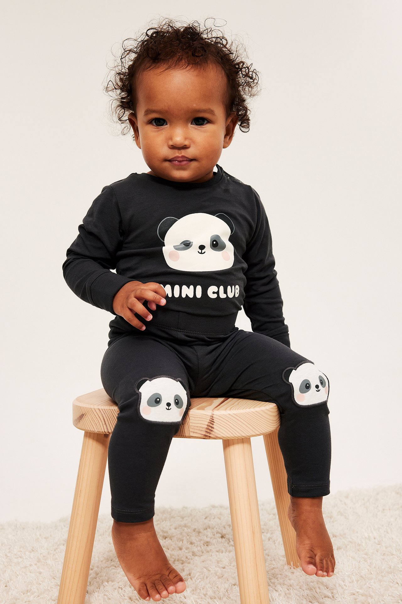 Forfra: baby i svart langermet body med pandatrykk og matchende svarte leggings med pandaknepatches.