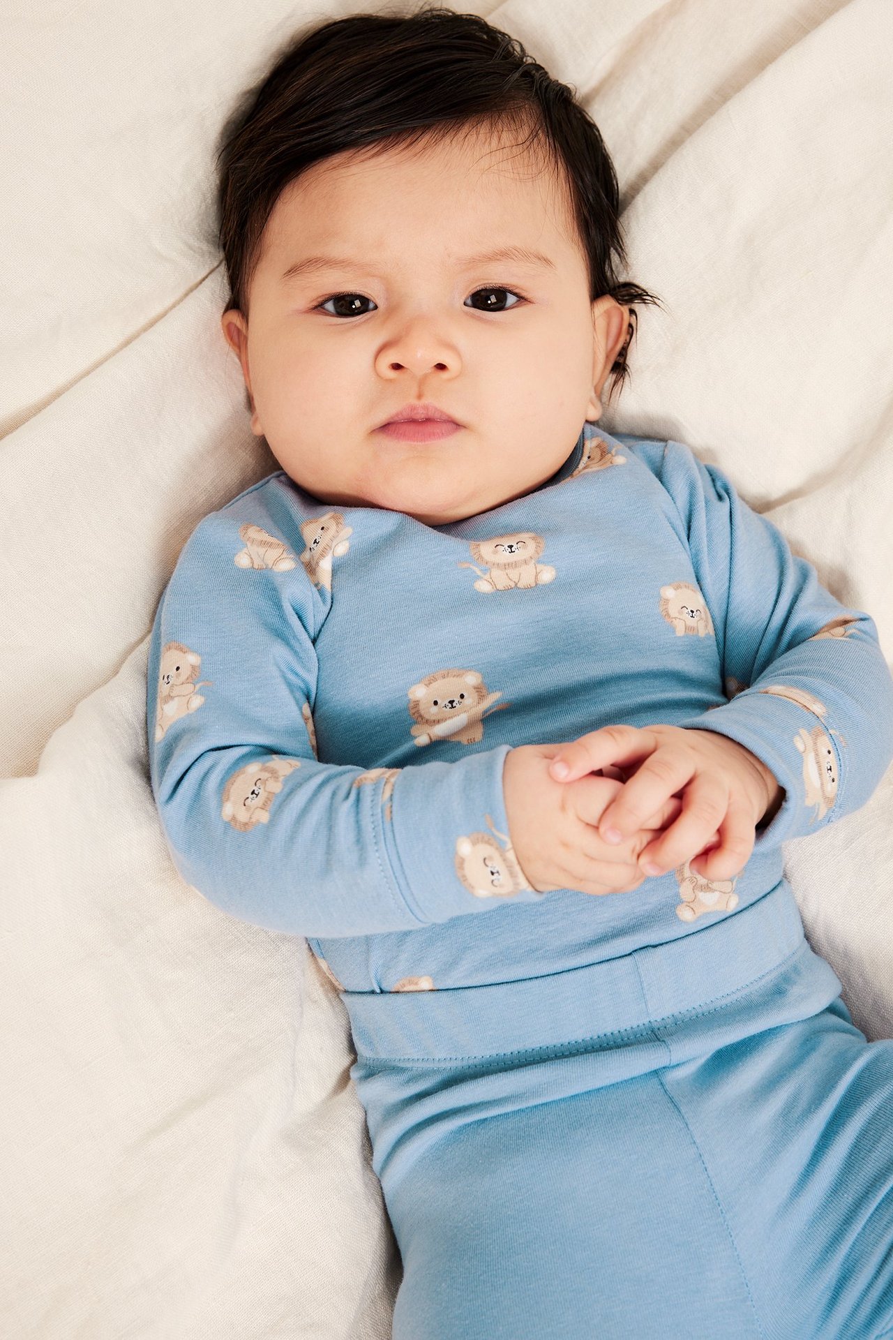 Ovanifrån: baby i ljusblå bomullsbody med heltäckande mönster av lejonungar.