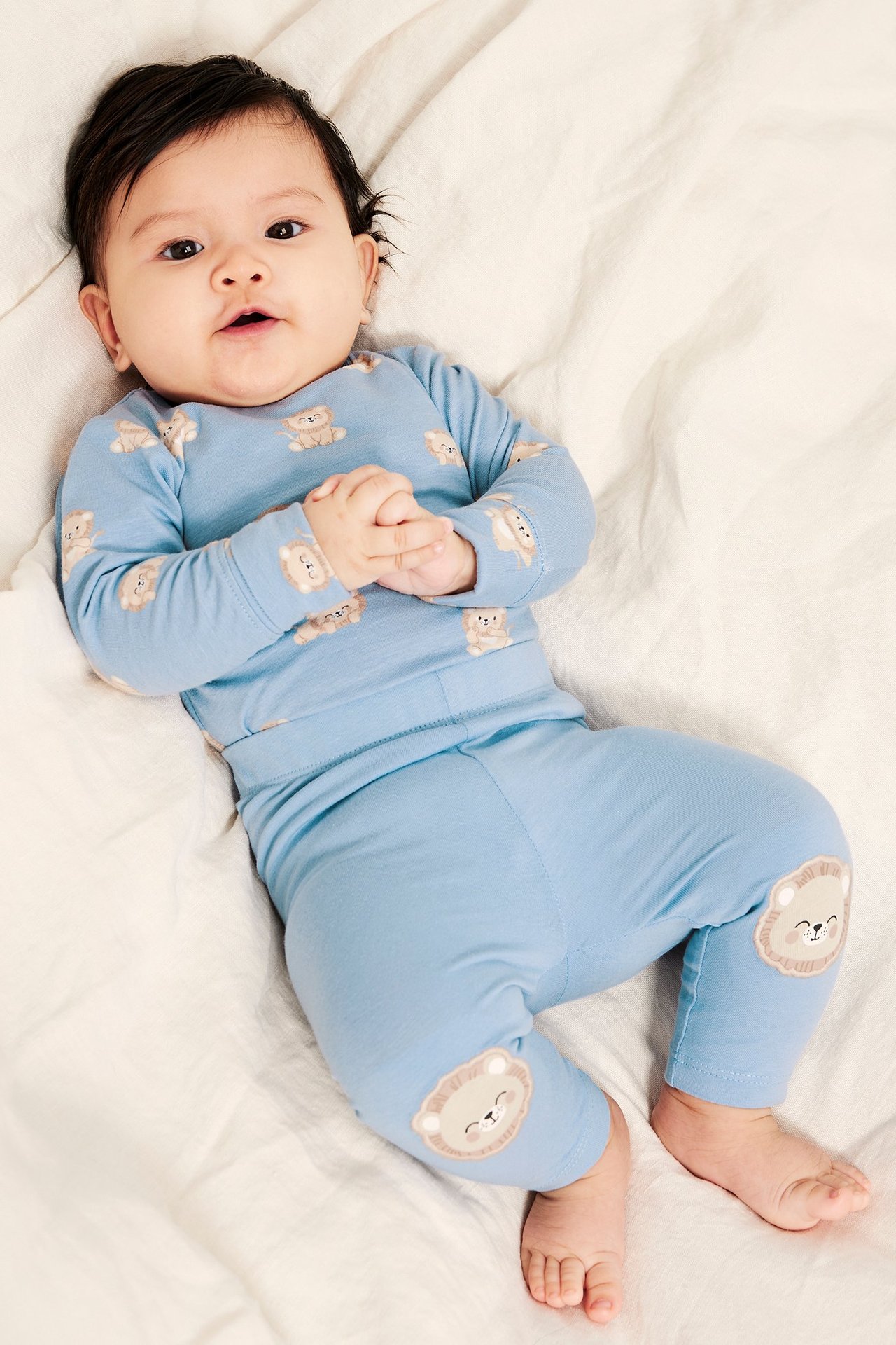 Toppvy av baby i ljusblå mönstrad body med tryckknappar och matchande byxor med djurmotiv på knäna.