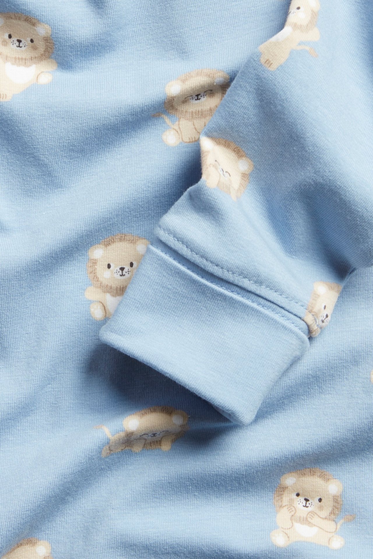 Zbliżenie na jasnoniebieskie body niemowlęce w lwy z podwiniętymi mankietami.