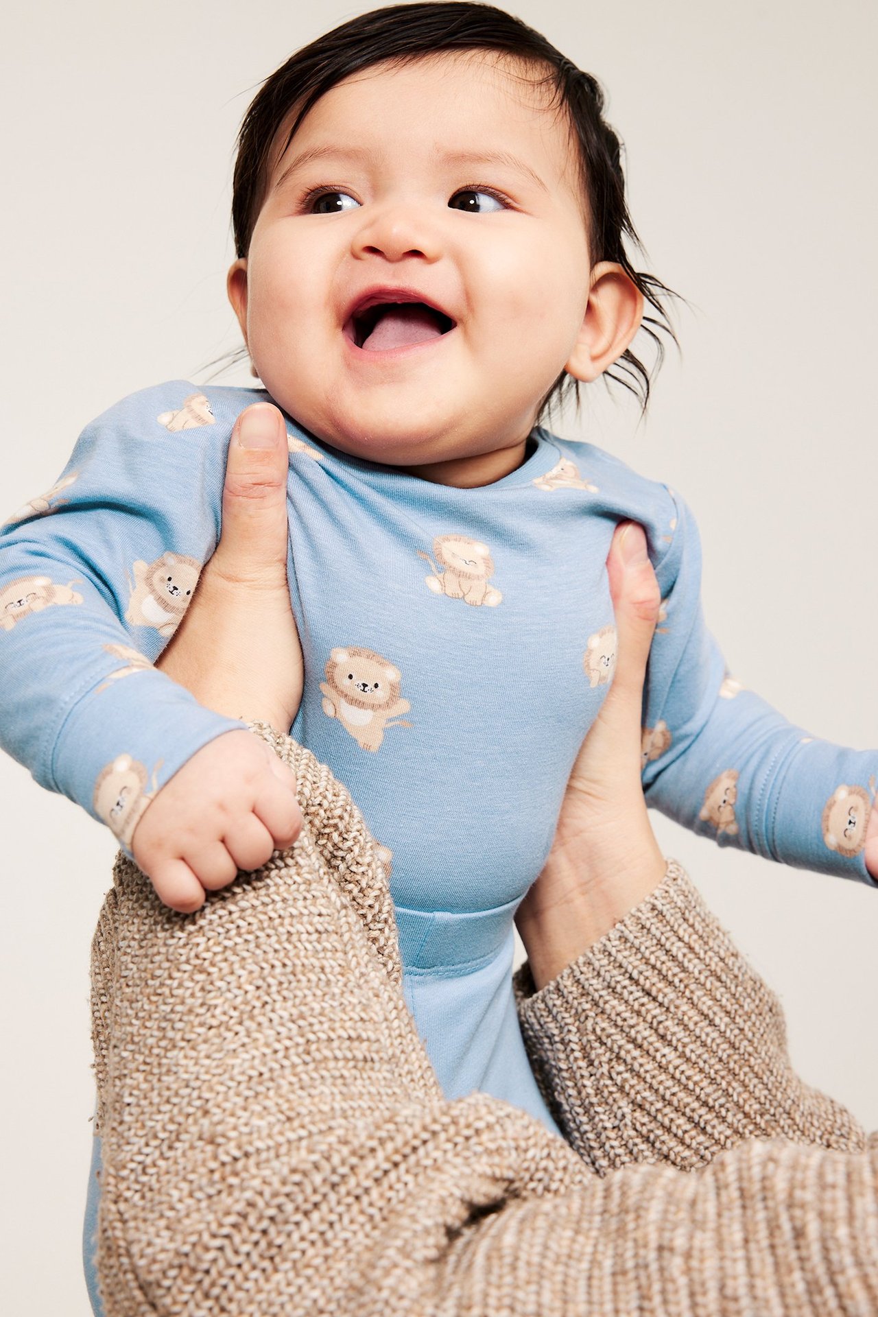 Närbild på glad baby i ljusblå bomullsbody med djurmönster, hållen av händer.
