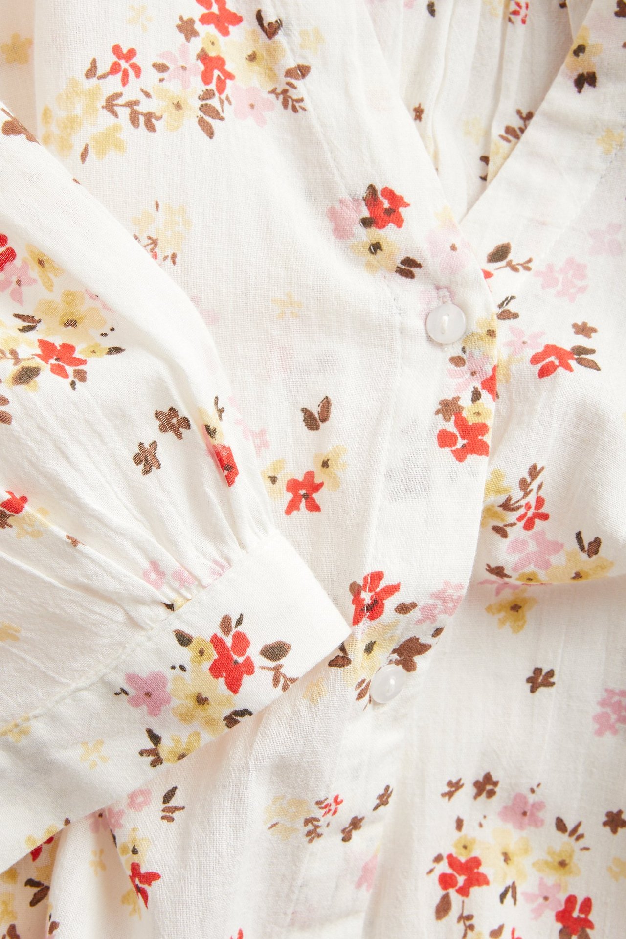 Zbliżenie: Biała, gnieciona sukienka bawełniana w kwiaty, dekolt w serek, guziki, mankiet.