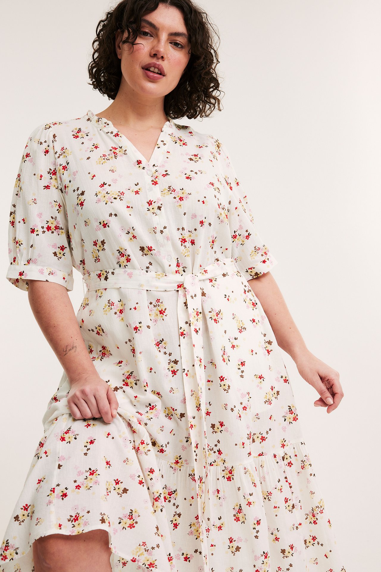 Framsida: Kvinna i offwhite mönstrad krinklad bomullsklänning med volanghals och knytskärp.