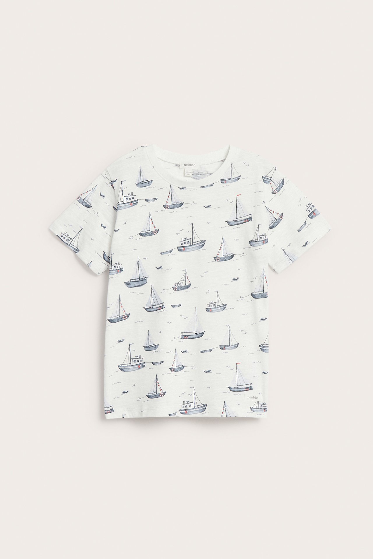 Framifrån en benvit kortärmad t-shirt i slubtrikå med ett heltäckande mönster av segelbåtar.