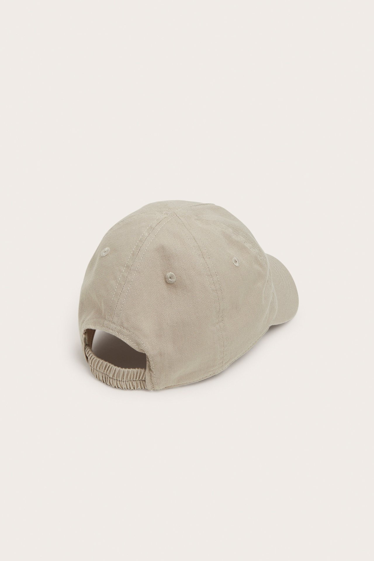 Bakfra en beige økologisk bomullscaps med broderi foran og strikk bak.