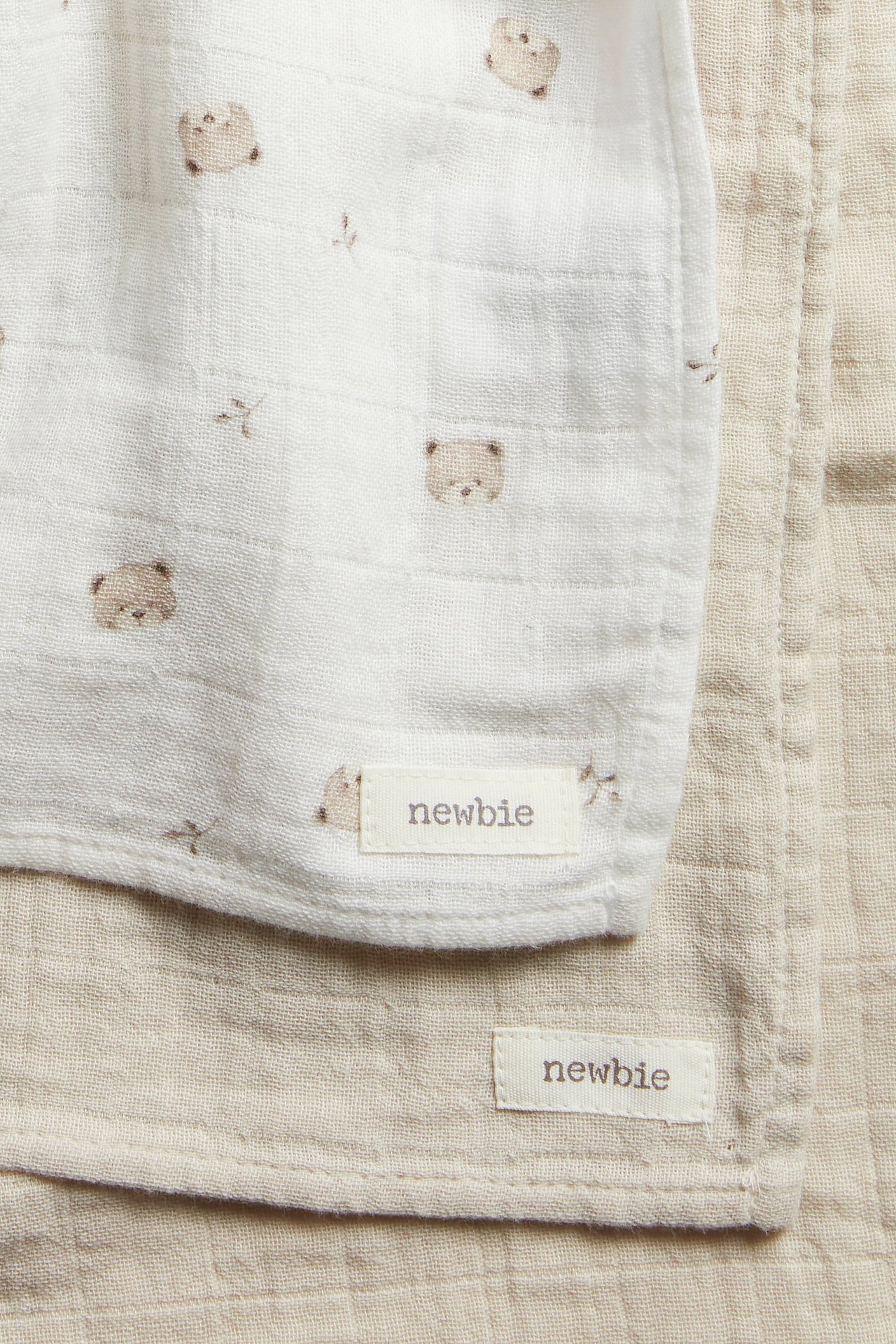 Zbliżenie dwóch bawełnianych kocyków muślinowych: jeden ecru w misie, drugi gładki jasnobeżowy.