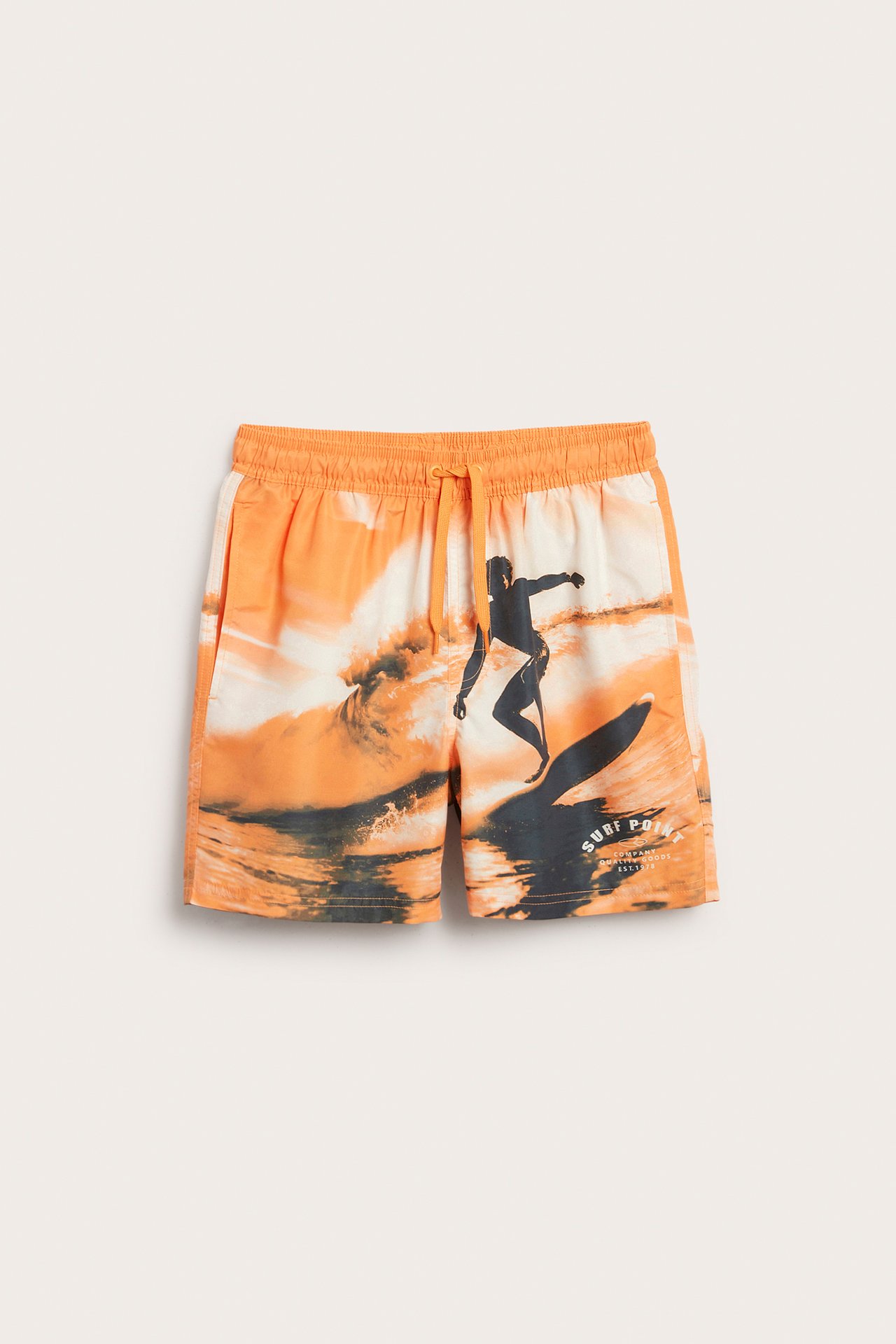 Framifrån: orange och vita vävda badshorts för barn med surfmönster och dragsko.