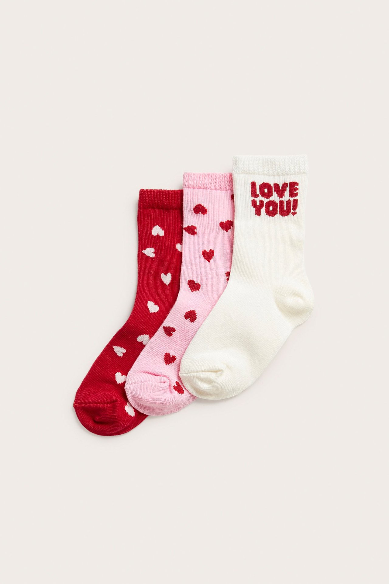 Trzy pary dziecięcych skarpetek. Ecru 'LOVE YOU!', różowe w czerwone serca, czerwone w białe serca.