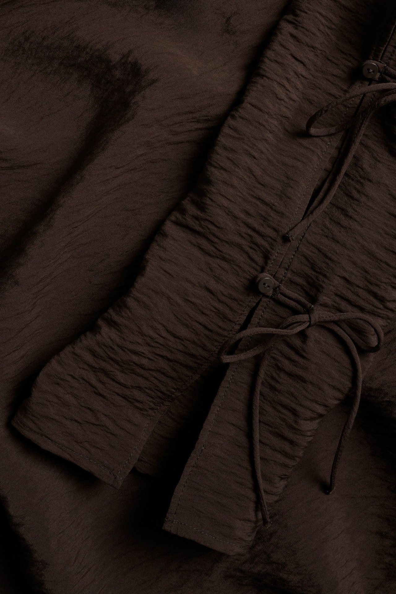 Zbliżenie ciemnobrązowej, marszczonej bluzki z mieszanki wiskozy z wiązanymi detalami na rękawie.
