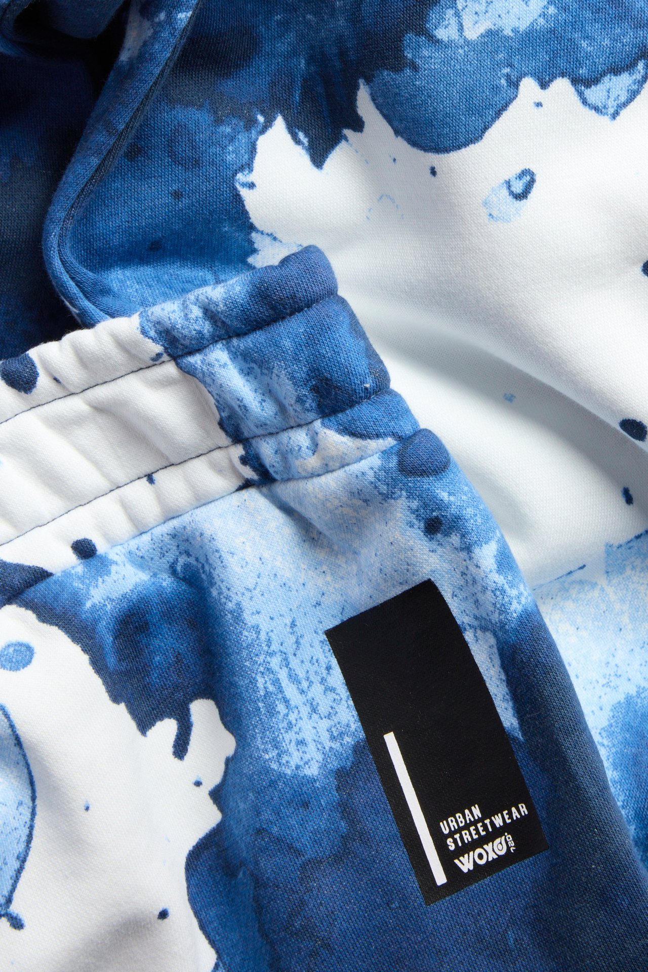 Zbliżenie na off-white spodnie dresowe z niebiesko-białym wzorem w plamy i elastycznym pasem.