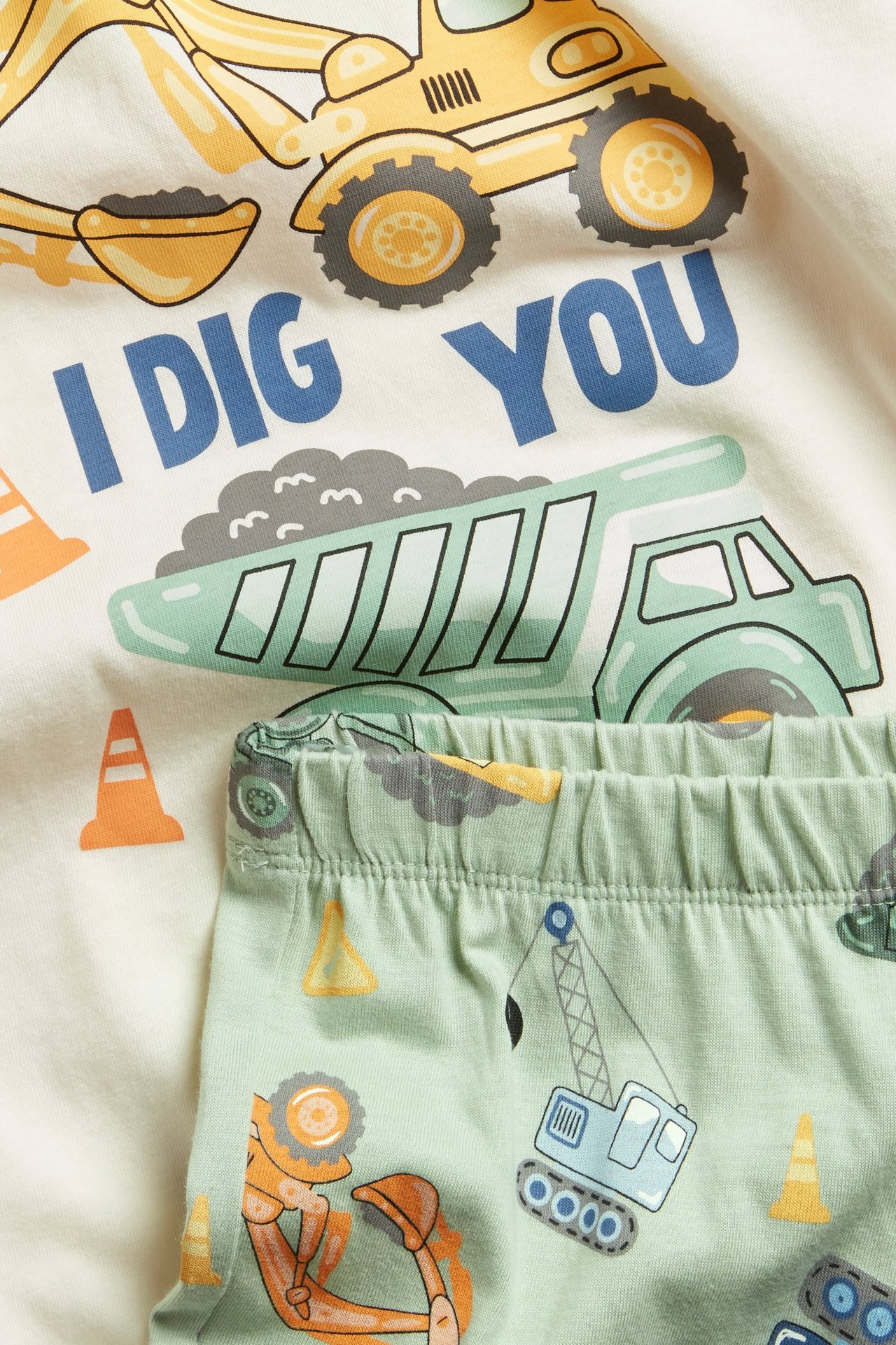 Zbliżenie: dziecięca piżama z naturalnej bawełny z nadrukiem pojazdów budowlanych i jasnozielone spodnie.