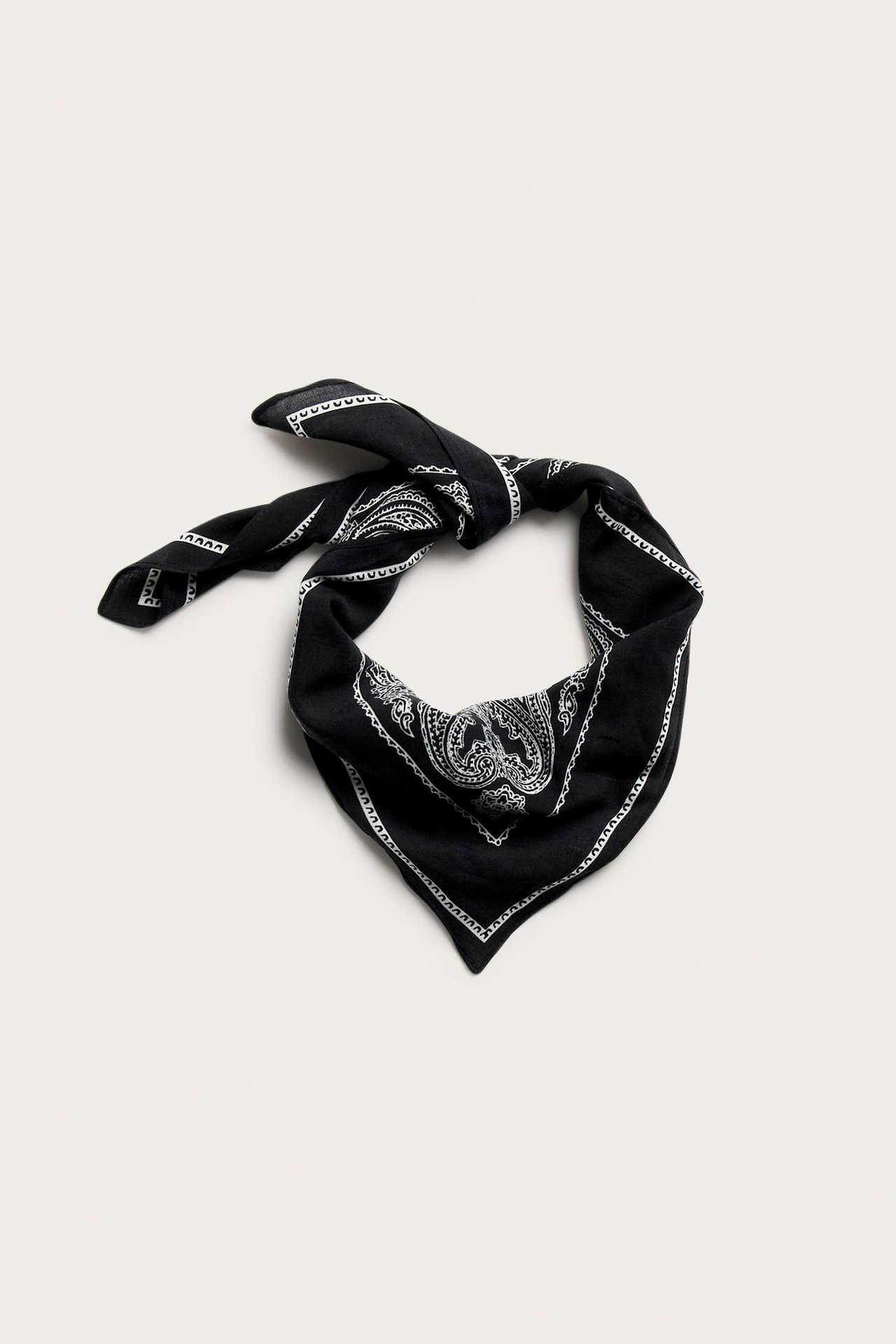 Litteästi aseteltu lähikuva: musta neliönmuotoinen paisleymönsterinen kierrätyspolyesterihuivi, solmittuna.