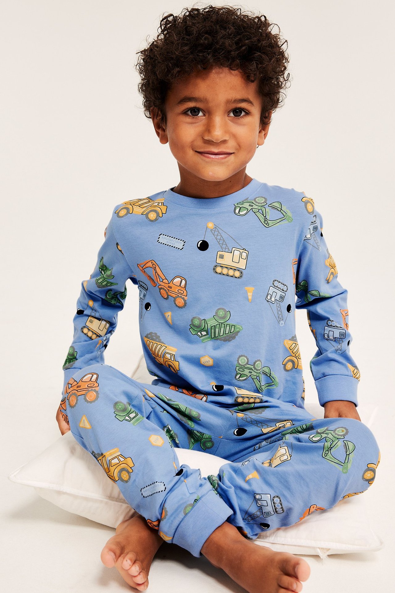 Edestä, poika yllään vaaleansiniset puuvillapyjamat rakennusajoneuvopainatuksella.