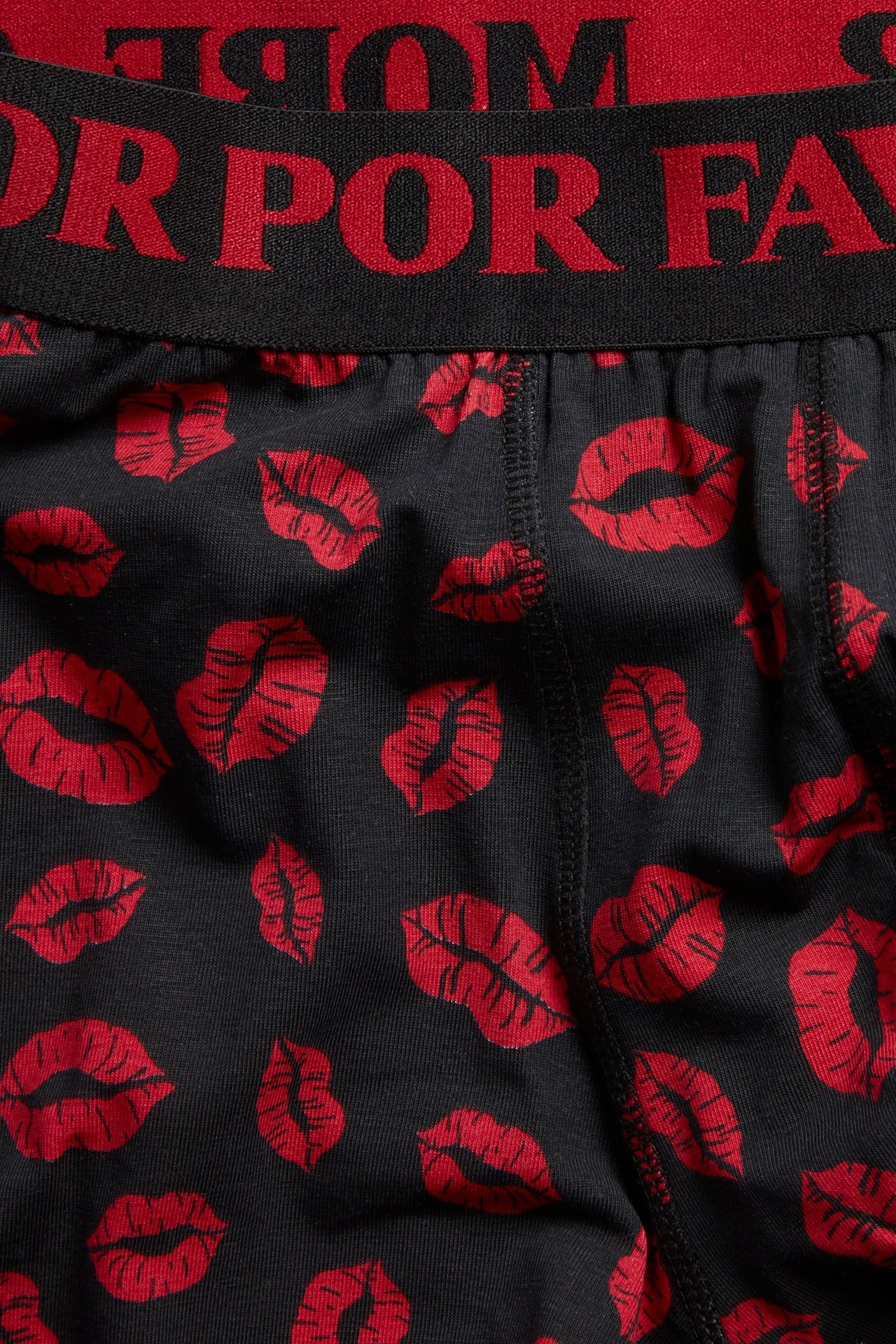 Zbliżenie na czarne bokserki męskie z czerwonym wzorem ust i czarnym pasem z czerwonym napisem.