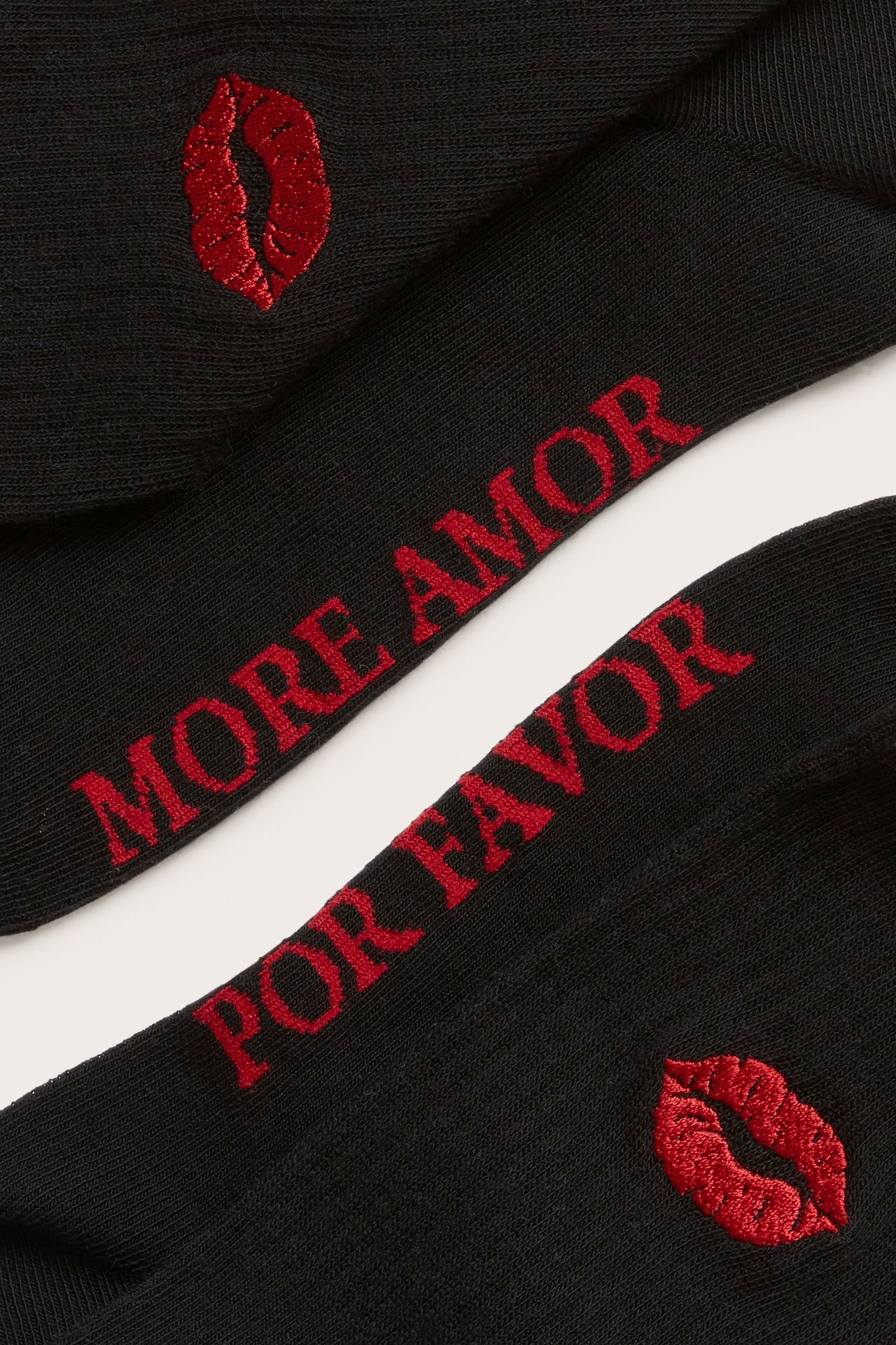Närbild av två svarta bomullsstrumpor med röd broderad text 'MORE AMOR POR FAVOR' och röda kyssmärken.