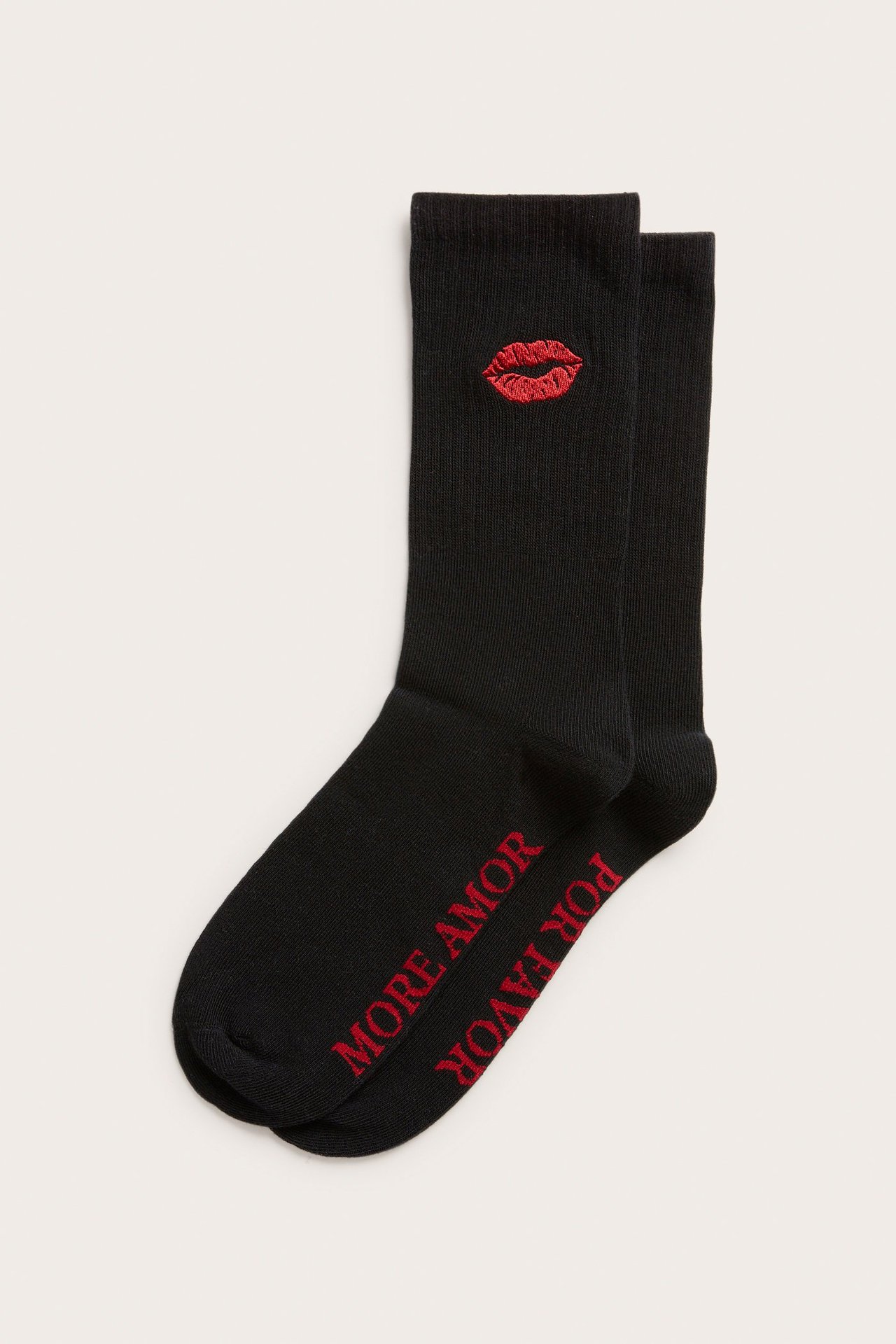 Framifrån, ett par svarta strumpor med röda broderade läppar och texten 'MORE AMOR POR FAVOR'.