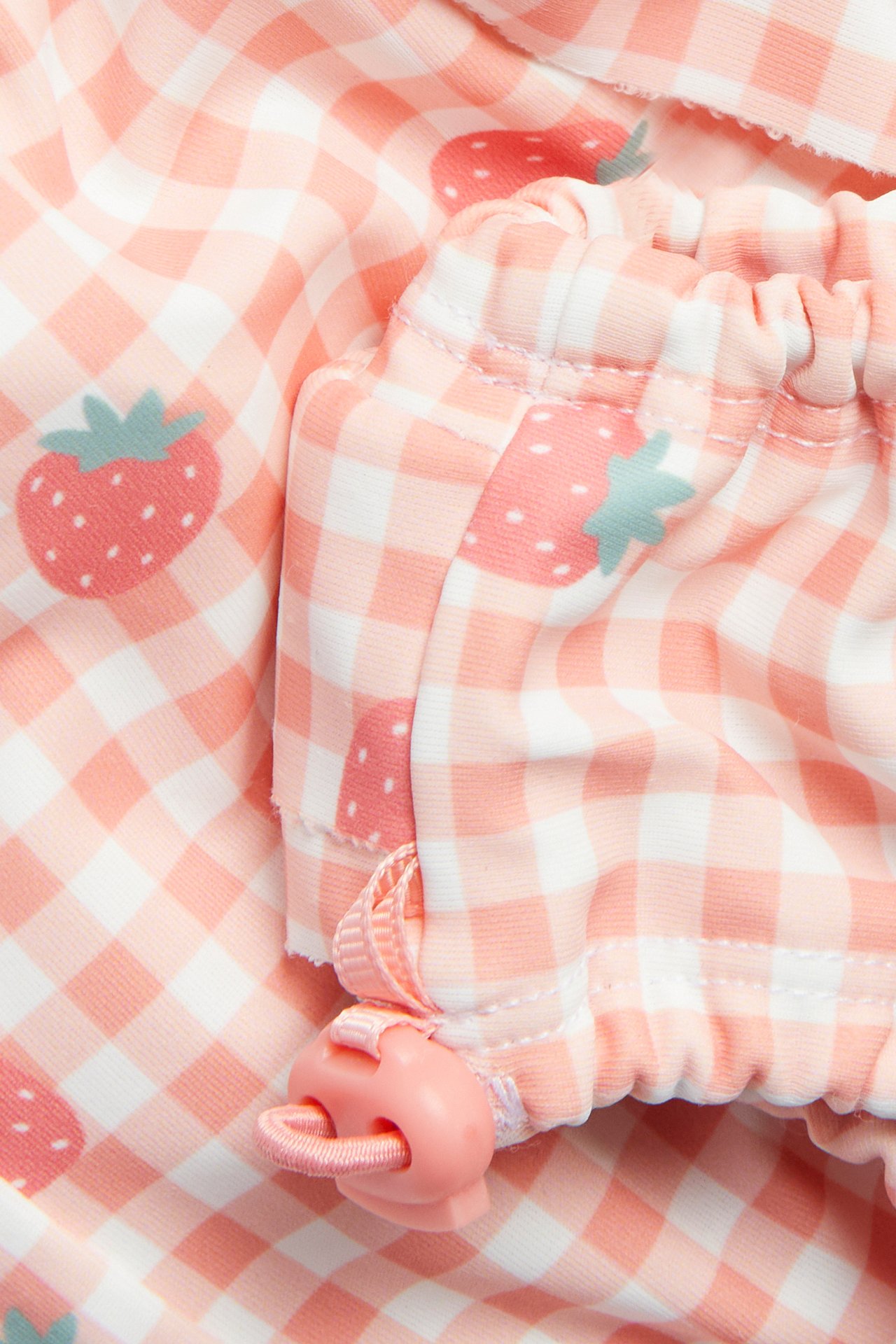 Närbild av babyrosa och vitrutiga badbyxor med jordgubbstryck och rosa dragsko med stopper.