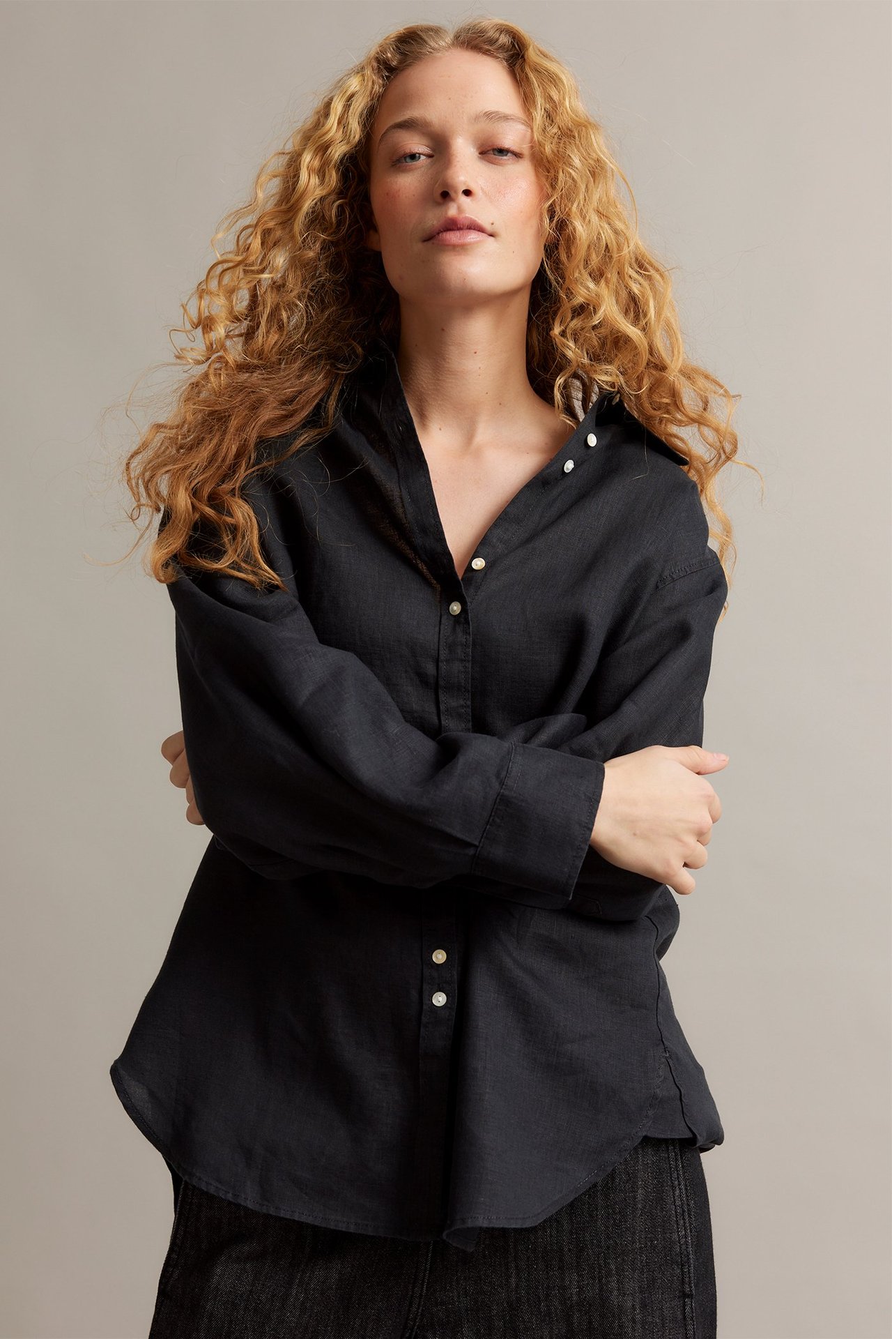 Widok z przodu: kobieta w luźnej czarnej koszuli lnianej z białymi guzikami perłowymi i ciemnych spodniach.