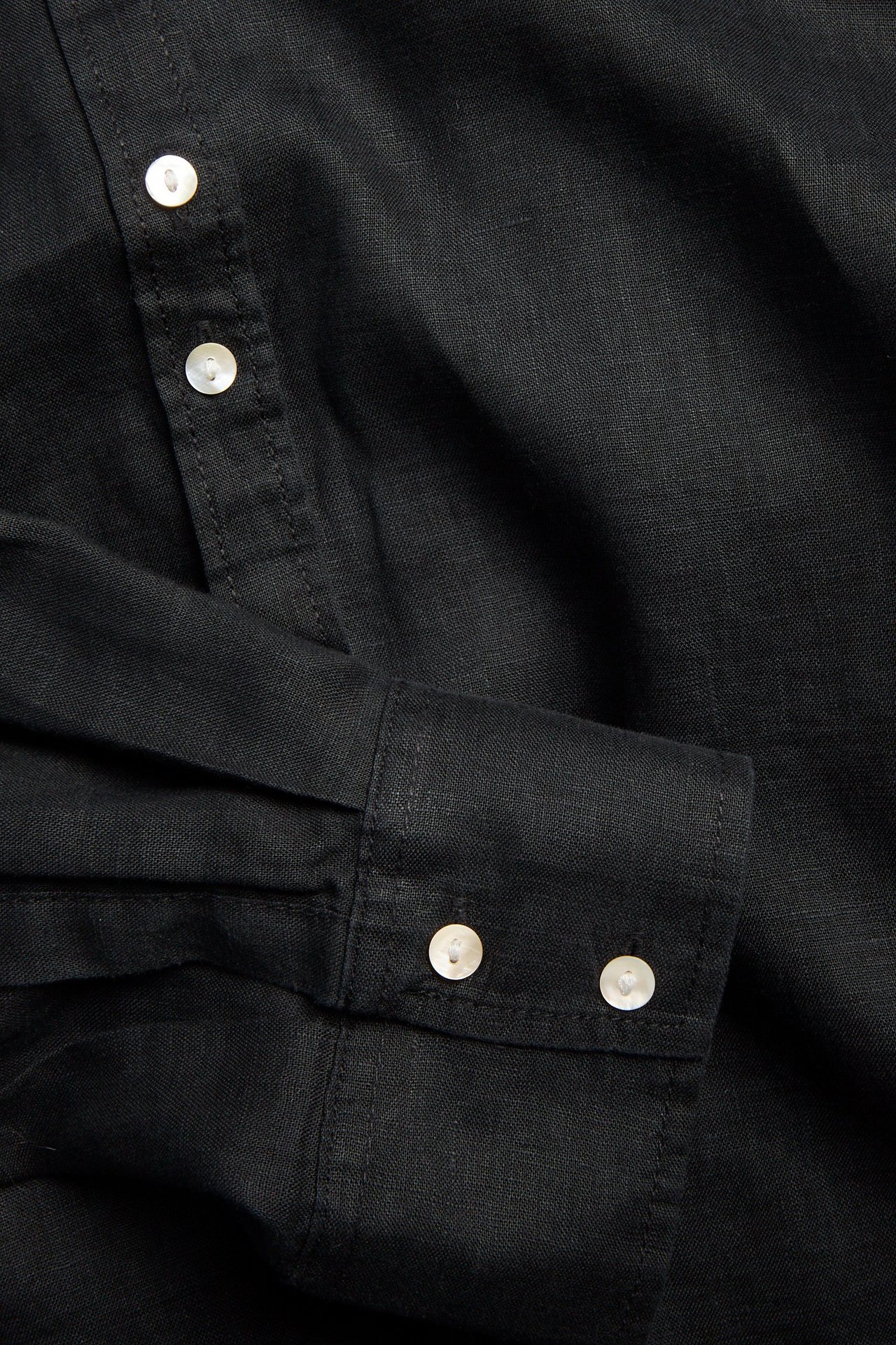 Zbliżenie czarnej lnianej koszuli z białymi guzikami z masy perłowej na plisie i mankiecie.