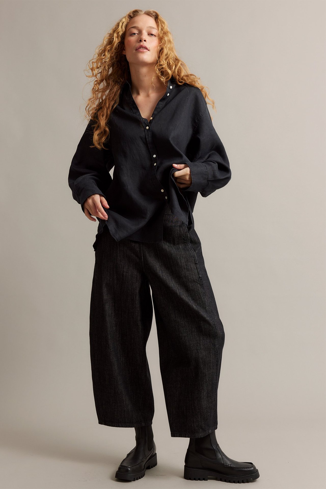 Widok z przodu: Kobieta w czarnej luźnej koszuli lnianej, czarnych szerokich spodniach i masywnych czarnych butach.