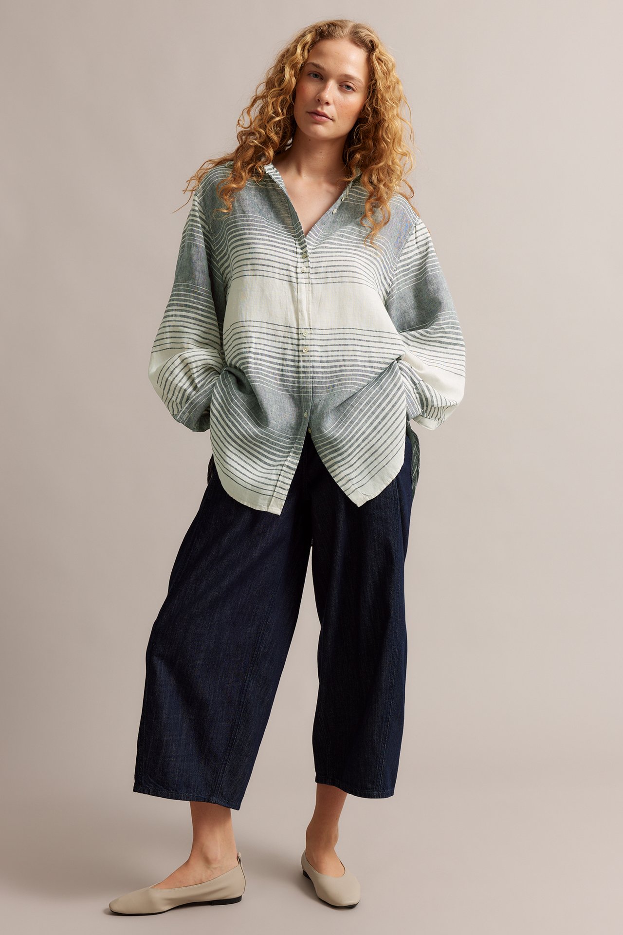 Forfra: Kvinne i en oversized lyseblå- og hvitstripet linskjorte, mørkeblå culottes og beige ballerinasko.