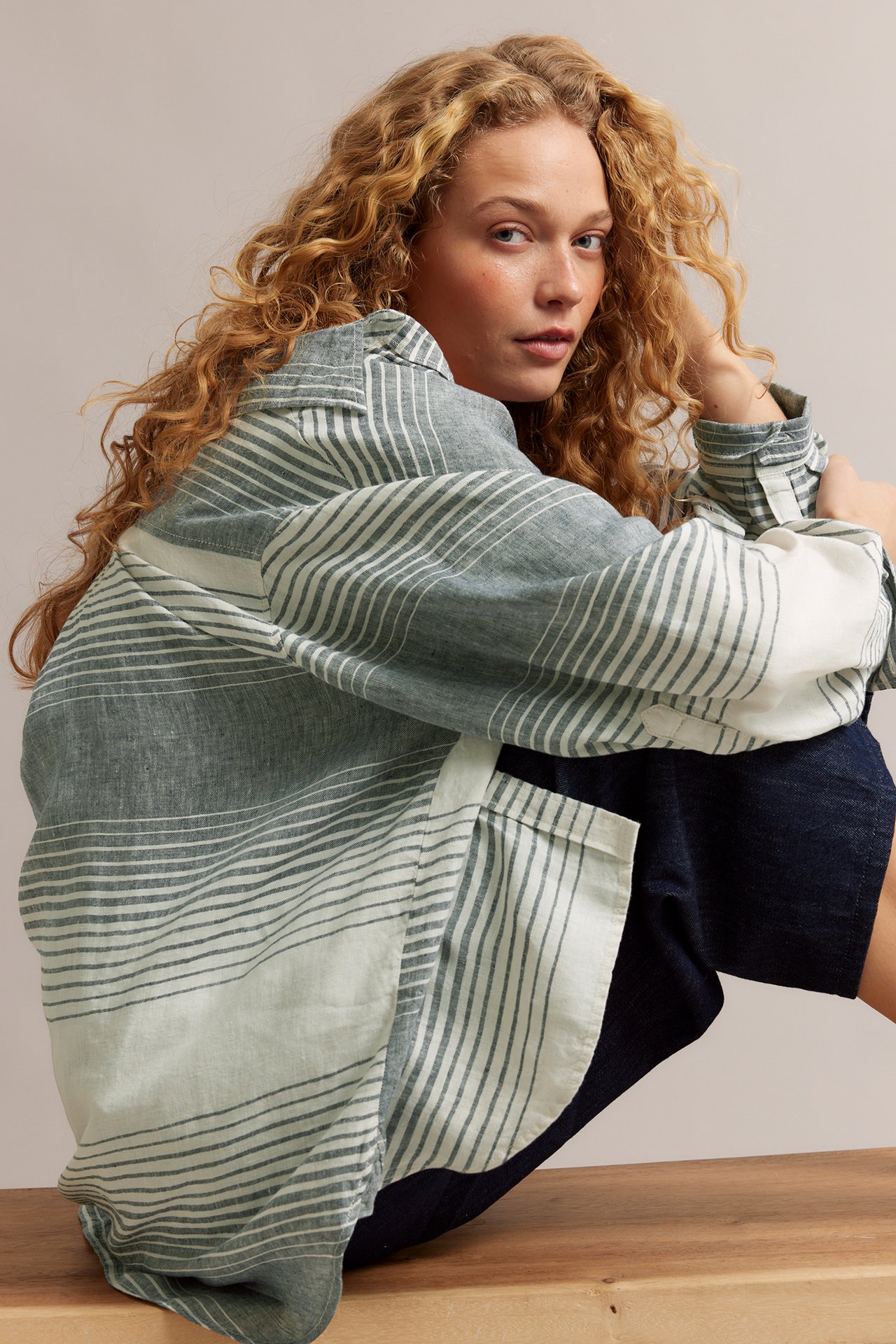 Närbild av en kvinna i en oversized mörkblå- och vitrandig linneskjorta och mörkblå shorts.