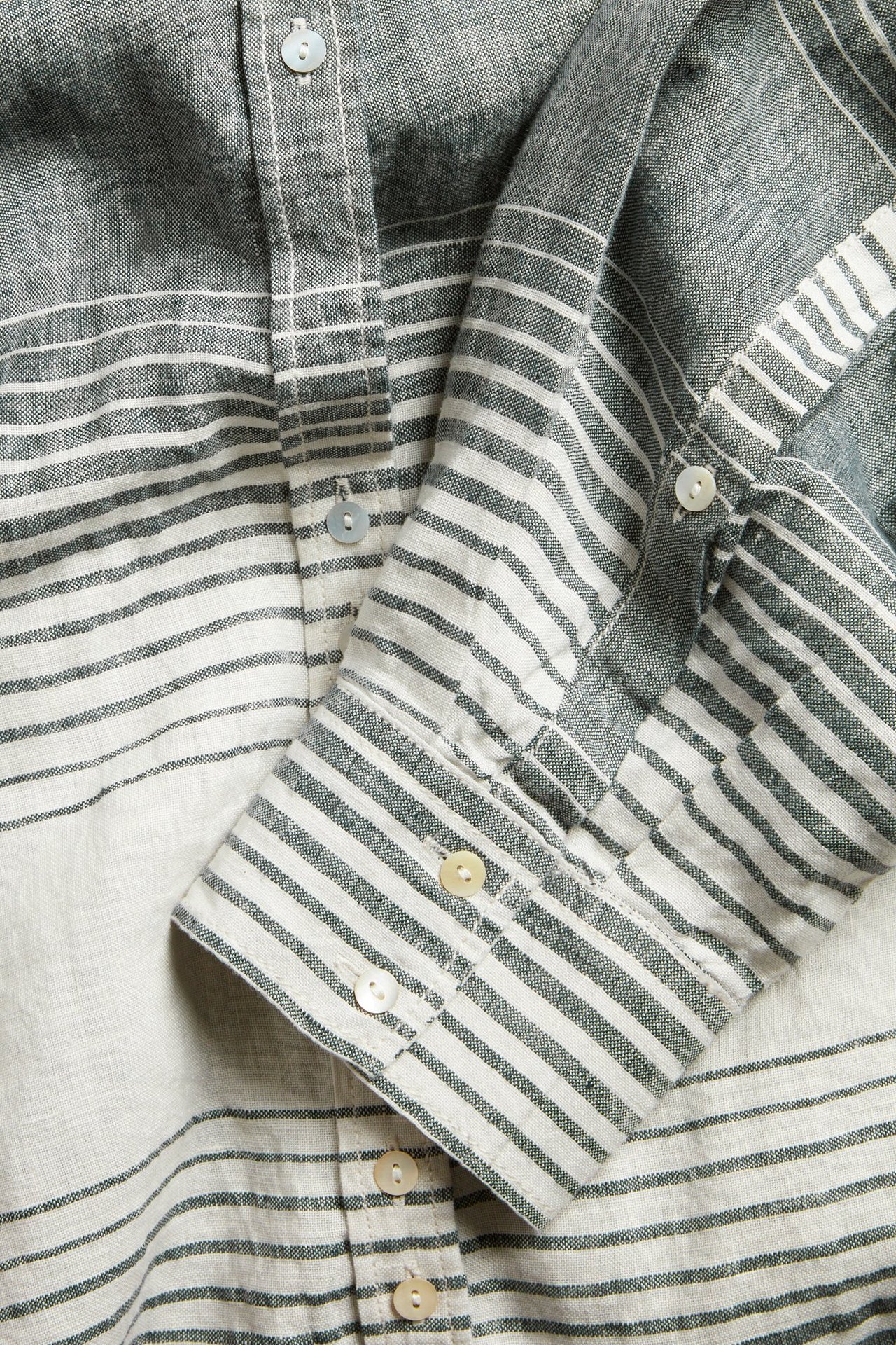 Zbliżenie na granatową koszulę lnianą w paski, z guzikami z masy perłowej na zapięciu i mankietach.