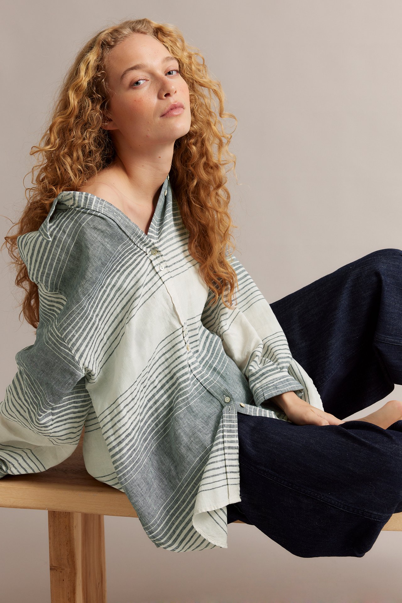 Kvinne i oversized blå/hvitstripet linskjorte med perlemorsknapper og mørkeblå bukser.