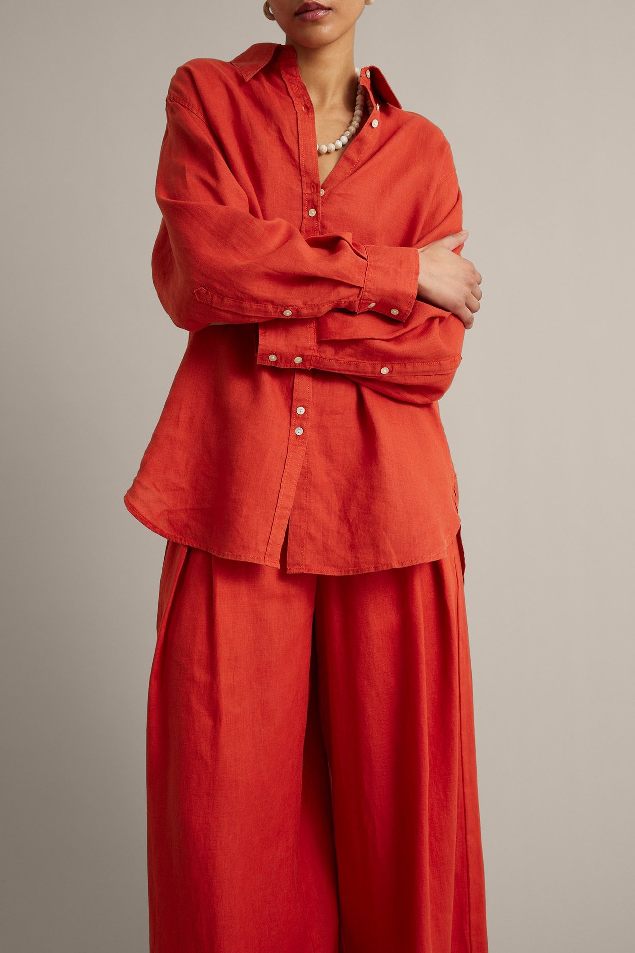 Forfra: Kvinne i rød linskjorte med perleknapper, matchende vide bukser og et perlekjede.