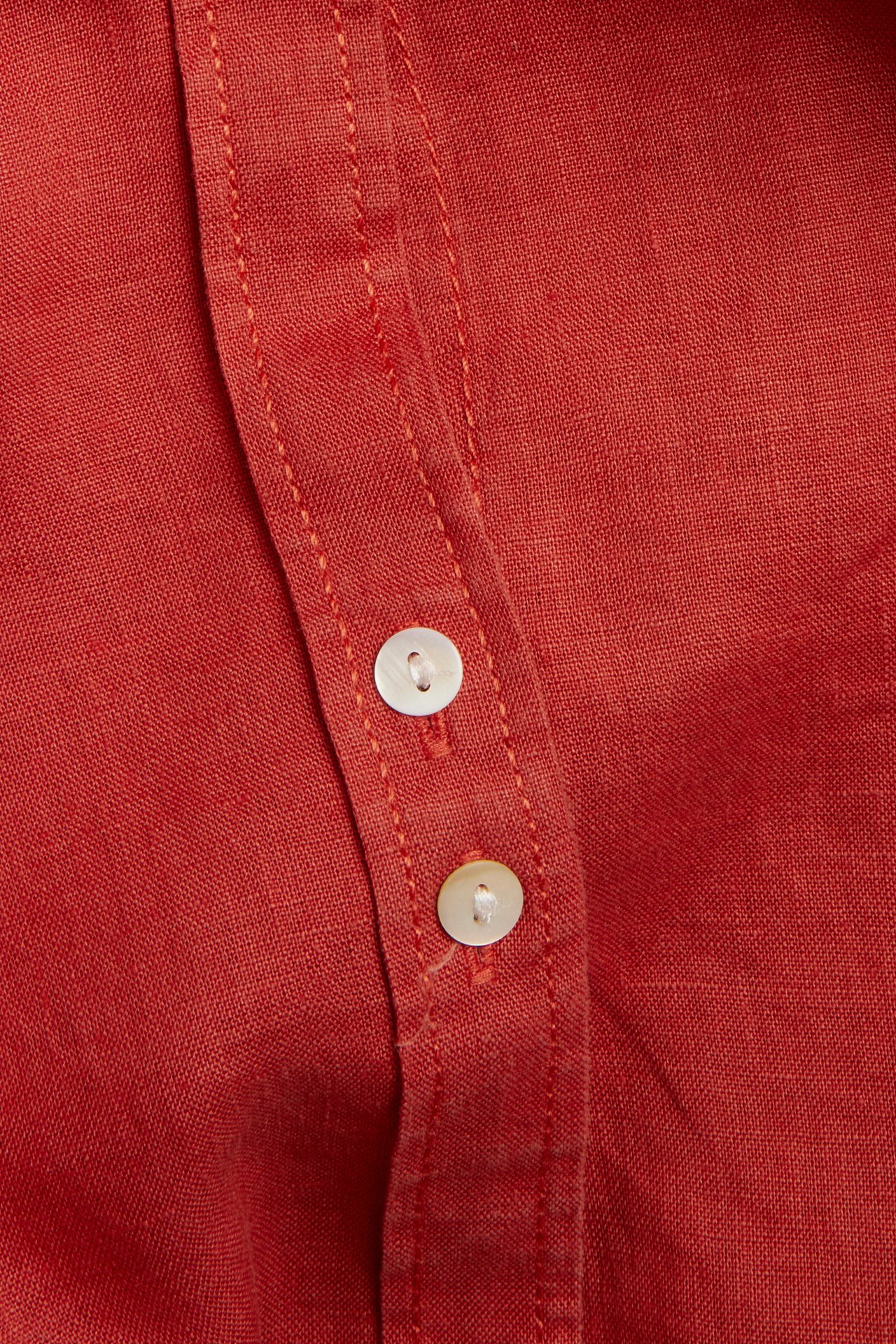 Zbliżenie czerwonej lnianej koszuli z dwoma guzikami z masy perłowej.