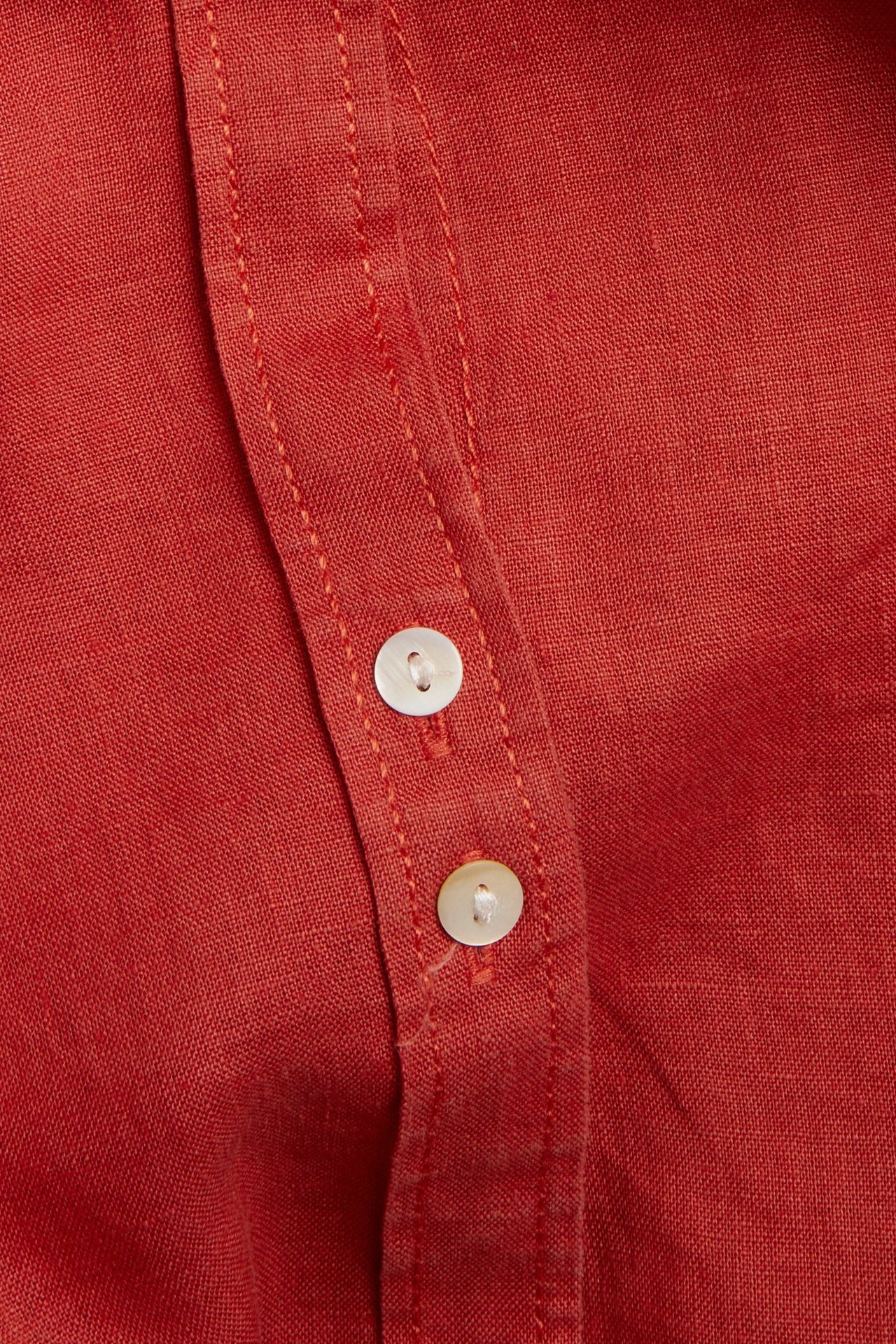 Nærbilde av en rød linskjorte med to perlemorknapper på knappingen.
