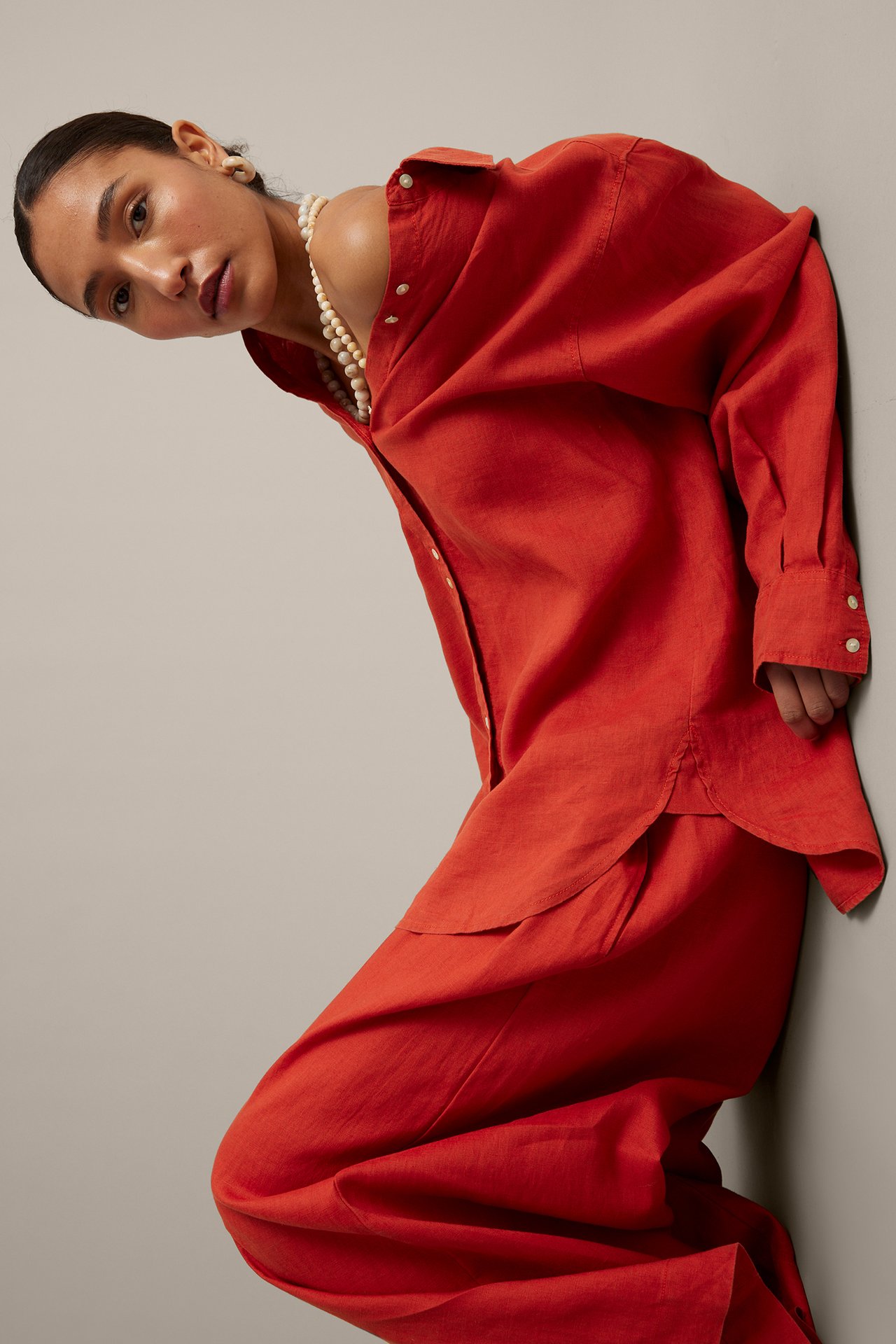 Kulmakuva naisesta yllään punainen ylisuuri pellavapaita, yhteensopivat housut, helmikaulakoru ja korvakoru.