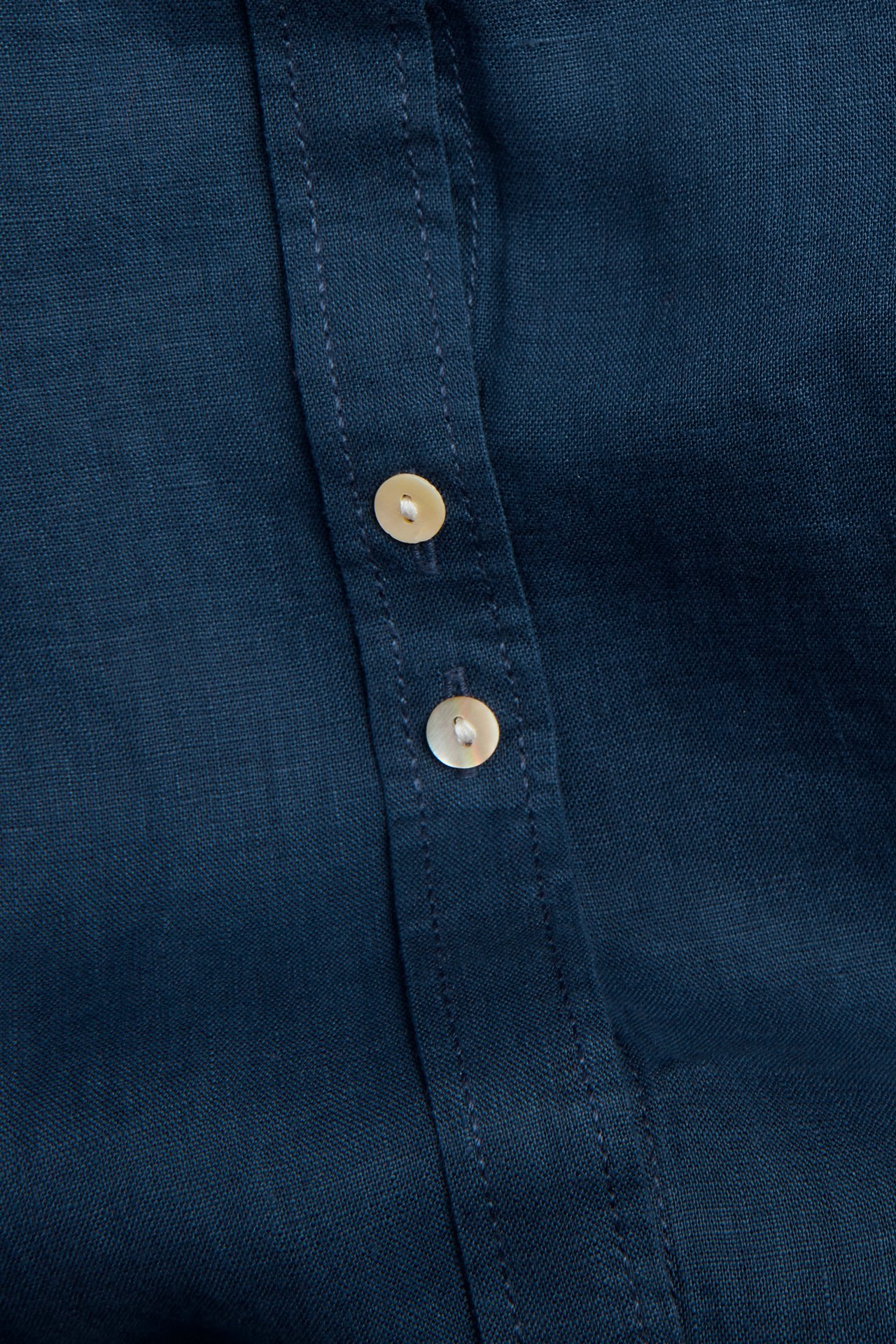 Zbliżenie granatowej lnianej koszuli z dwoma jasnymi guzikami z masy perłowej na plisie.