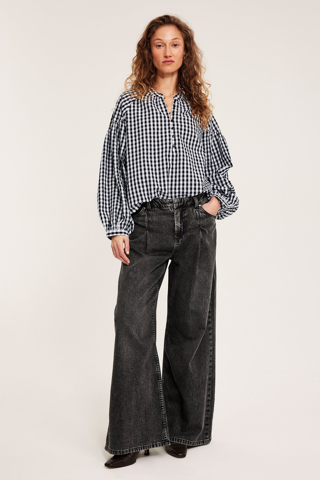 Frontalvisning: Kvinne i svart og hvit rutete seersuckerbluse og mørkegrå vide jeans.