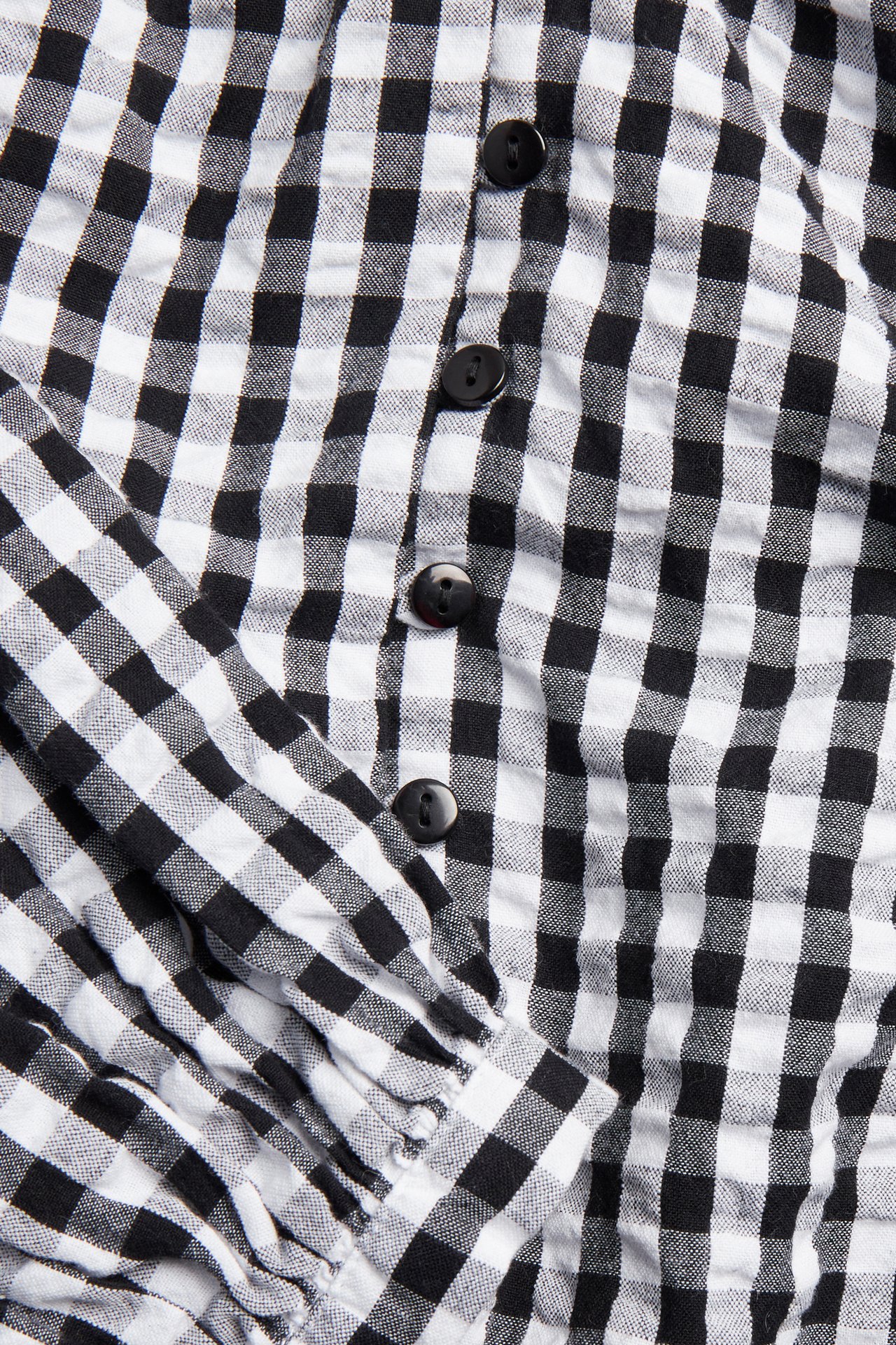 Nærbilde av en svart- og hvitrutete seersuckerbluse med knapper foran og rynket erme.