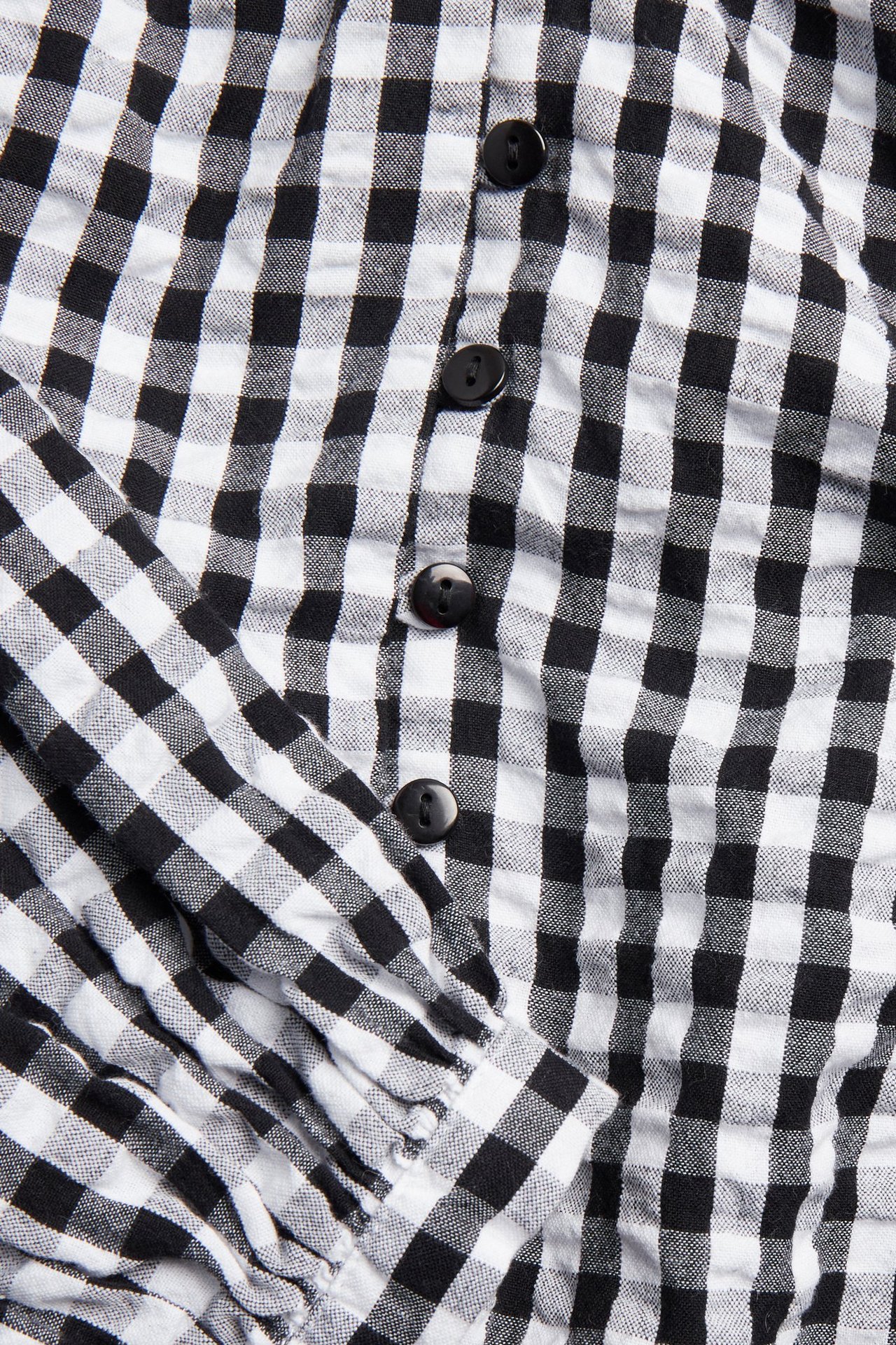 Zbliżenie na czarno-białą bluzkę w kratę z bąbelkowej bawełny z guzikami z przodu i marszczonym rękawem.