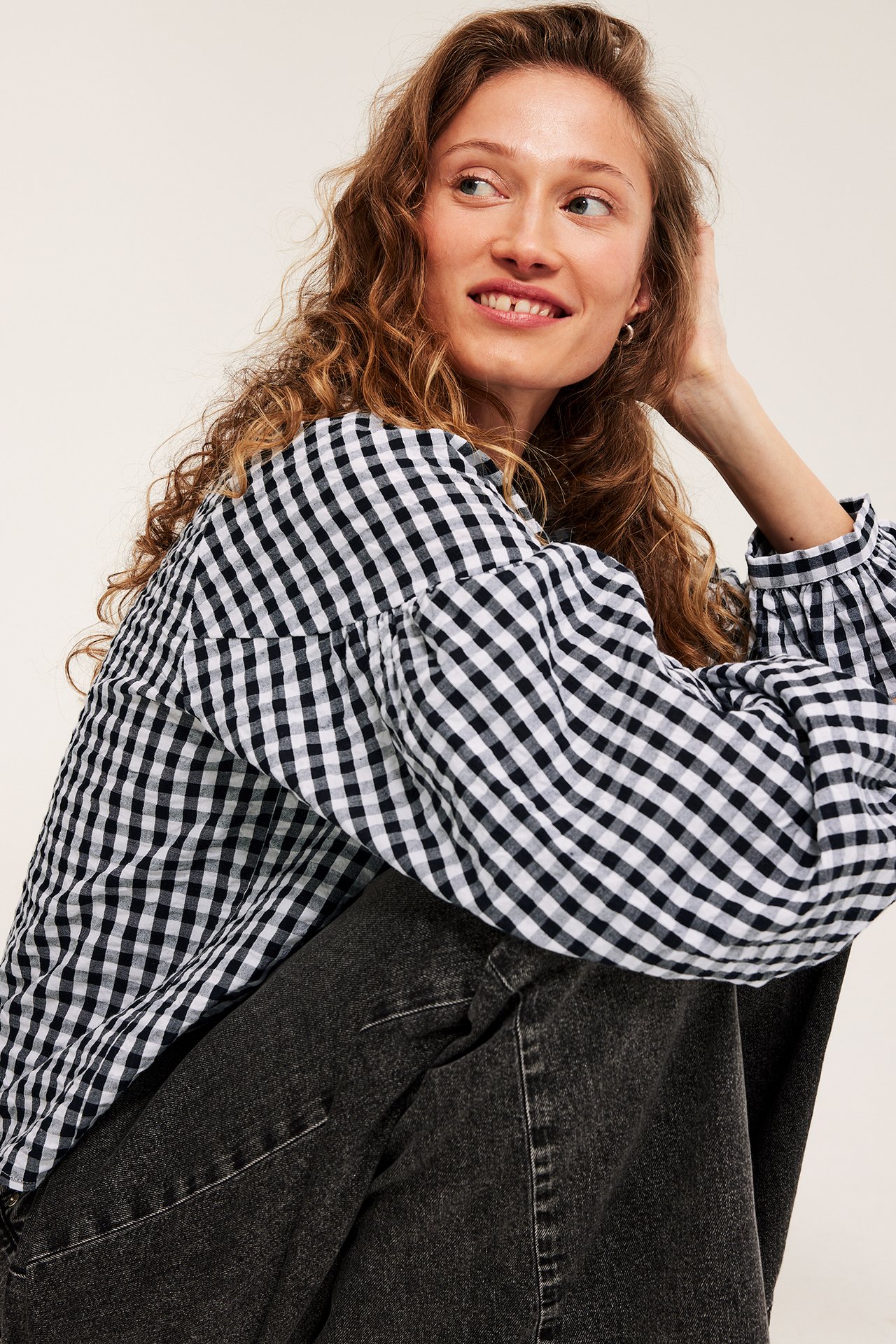 Nærbilde av kvinne i svart-hvit rutete seersucker-bluse med puffermer og mørkegrå jeans.