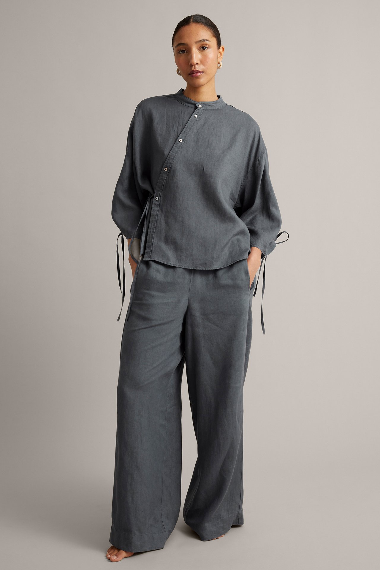 Frontvy av en kvinna i mörkblå linneblus med snedknäppning och matchande vida linnebyxor.