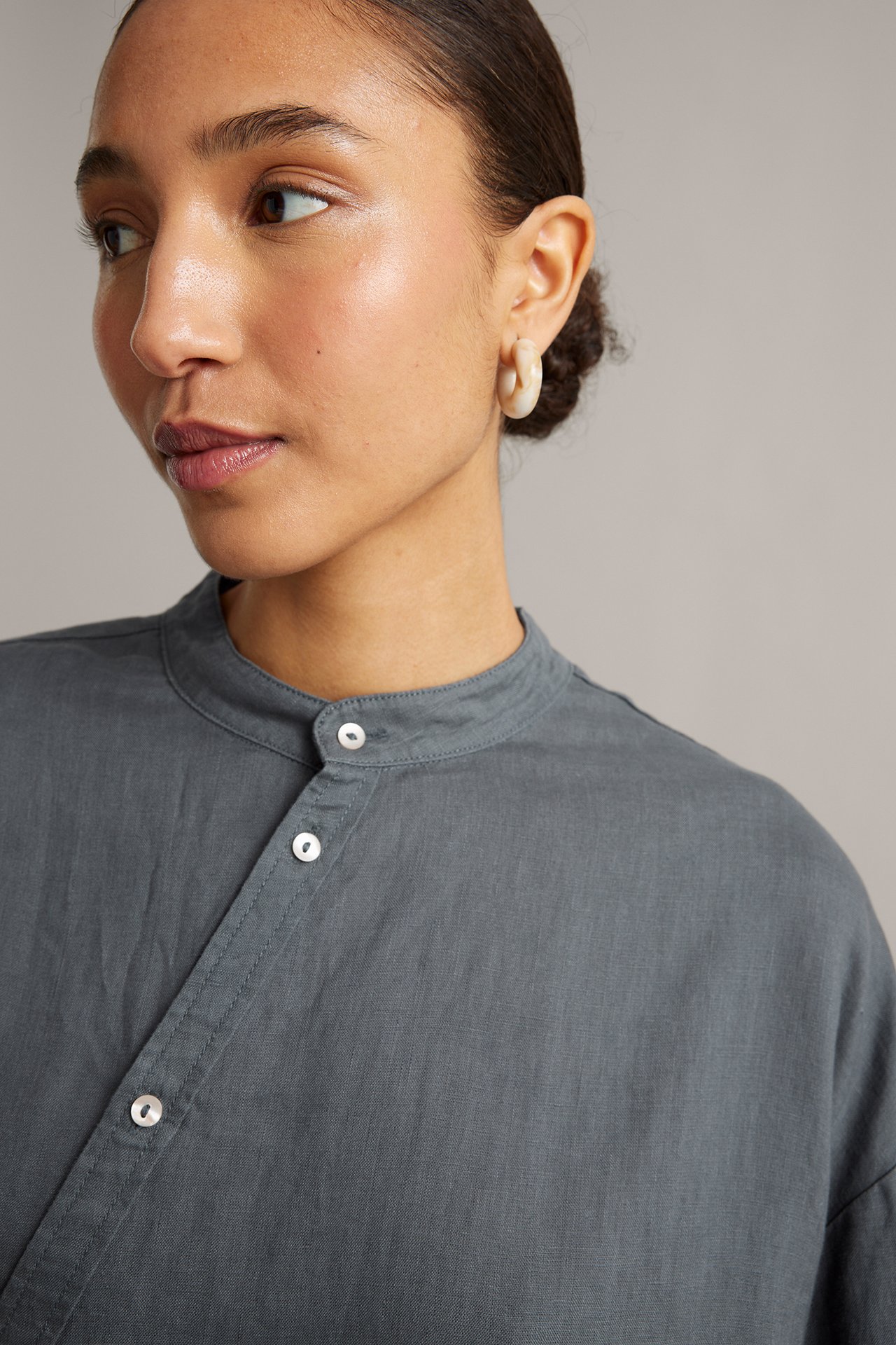 Nærbilde forfra av en kvinne i blå linbluse med skrå knapperad og beige ringøredobber.