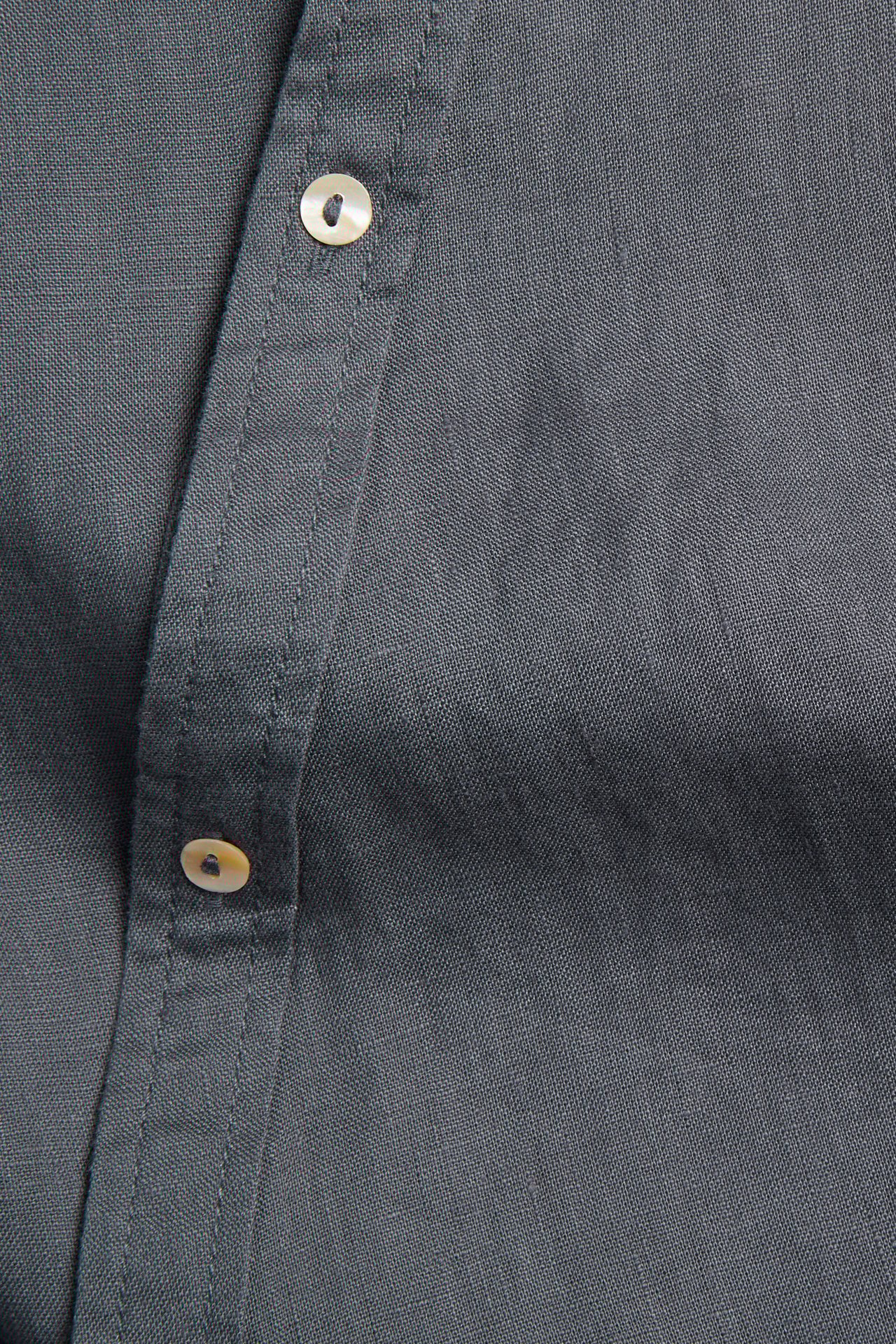 Nærbilde av en mørkeblå linbluse med knappestolpe og lyse knapper.