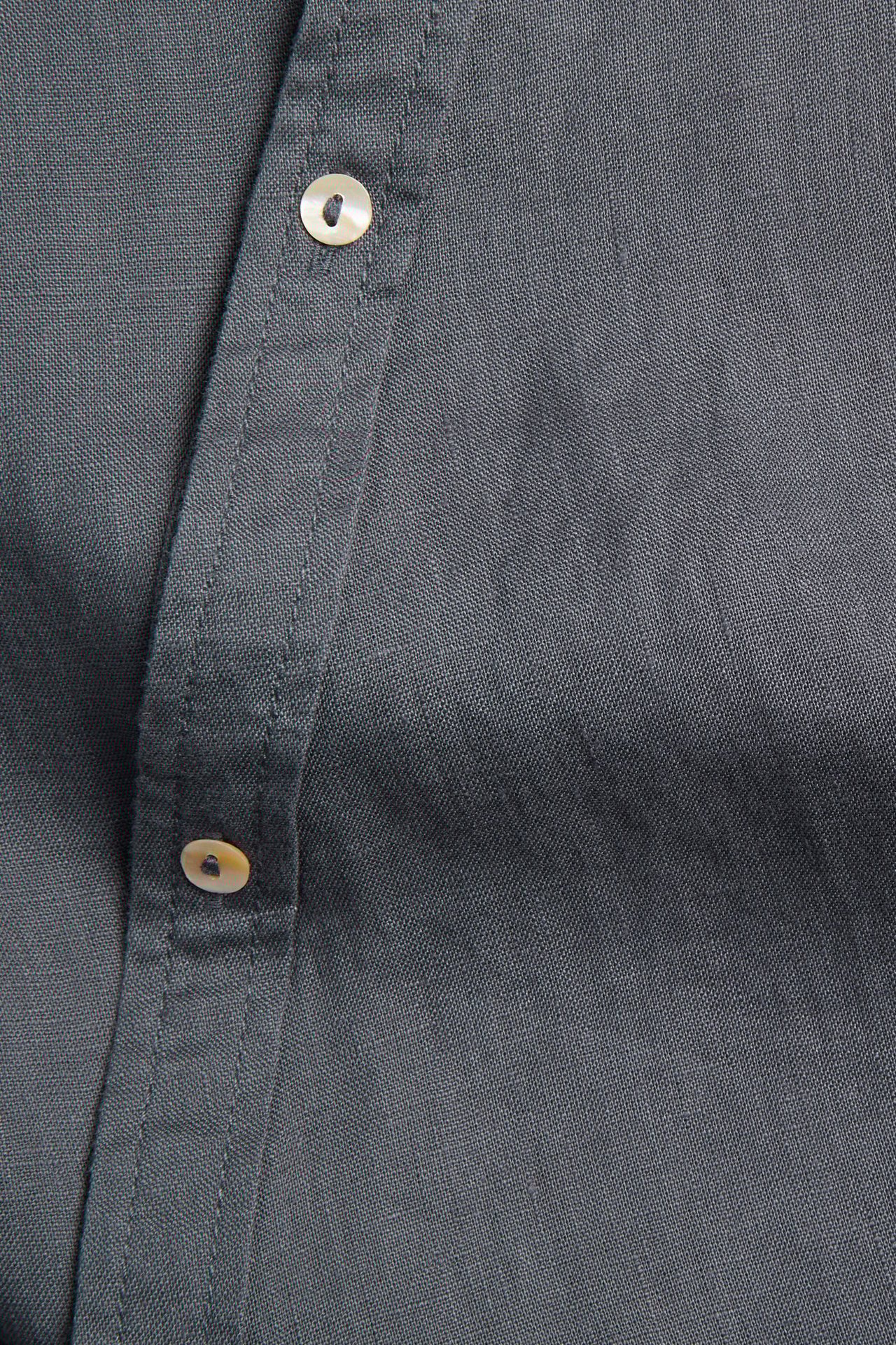 Nærbilde av en mørkeblå linbluse med knappestolpe og lyse knapper.