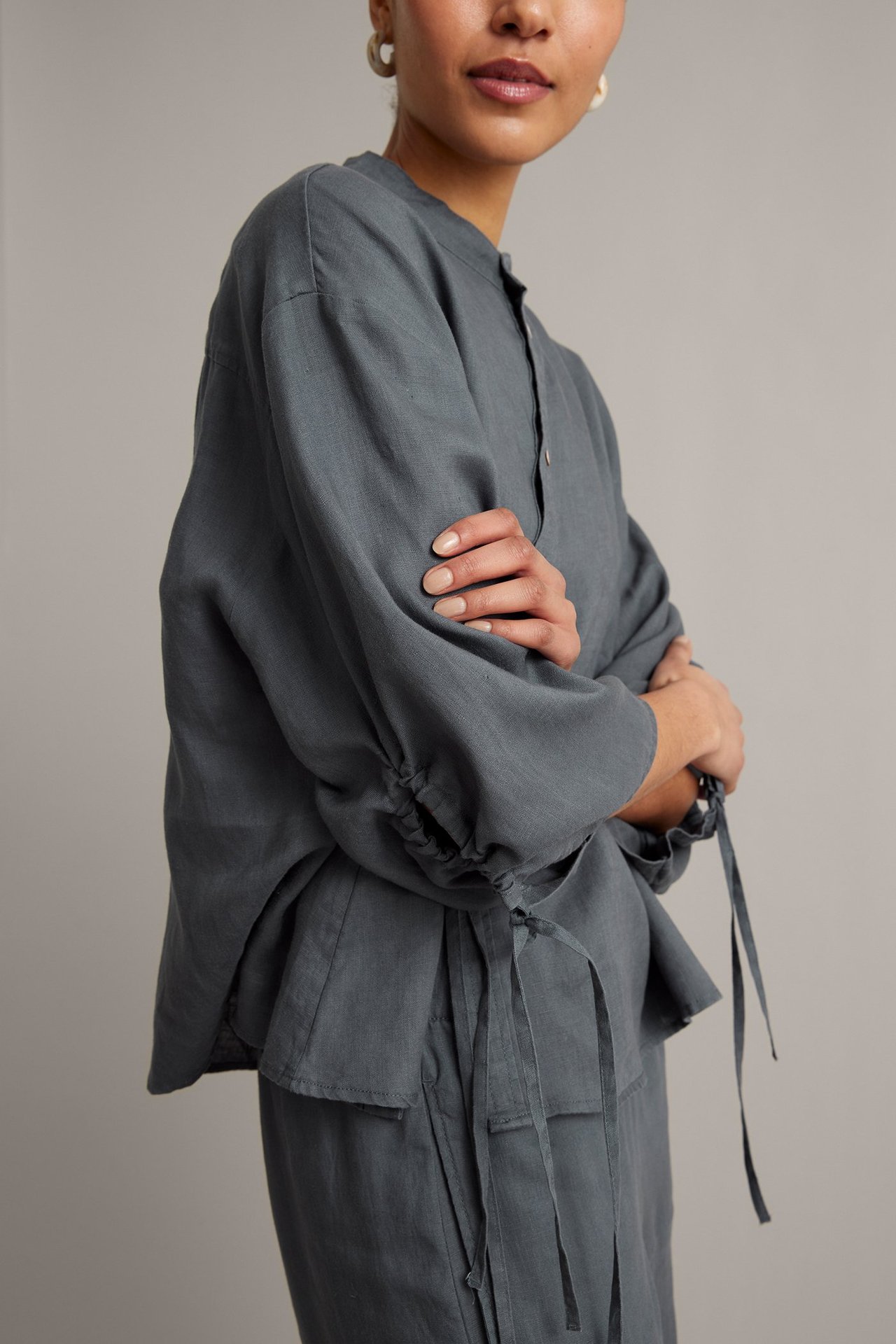 Widok z przodu: kobieta w luźnej ciemnoniebieskiej lnianej bluzce ze stójką, ukośnymi guzikami i ściągaczami.