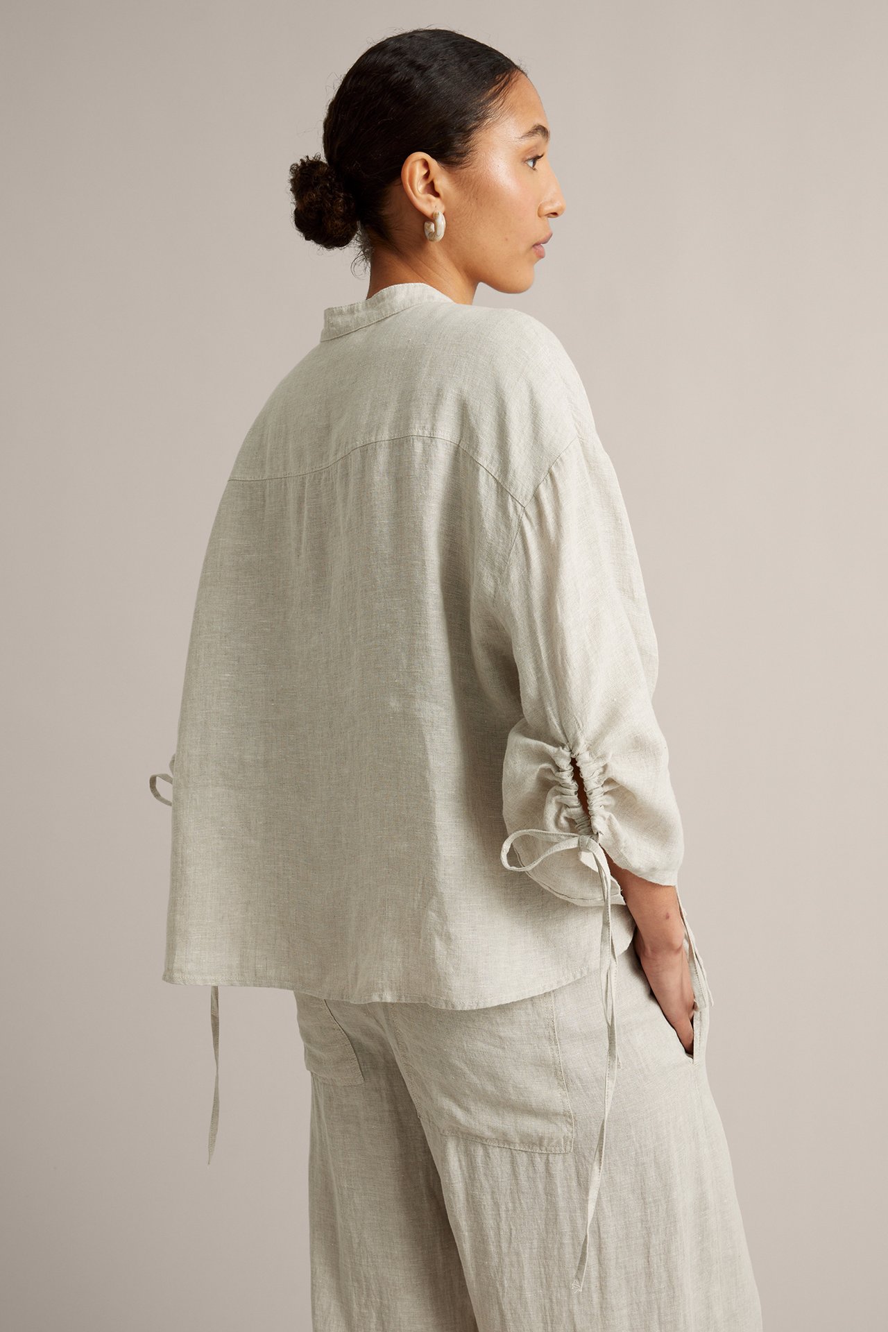 Bakfra-siden av en kvinne i beige linbluse med snorermer og matchende linbukser.